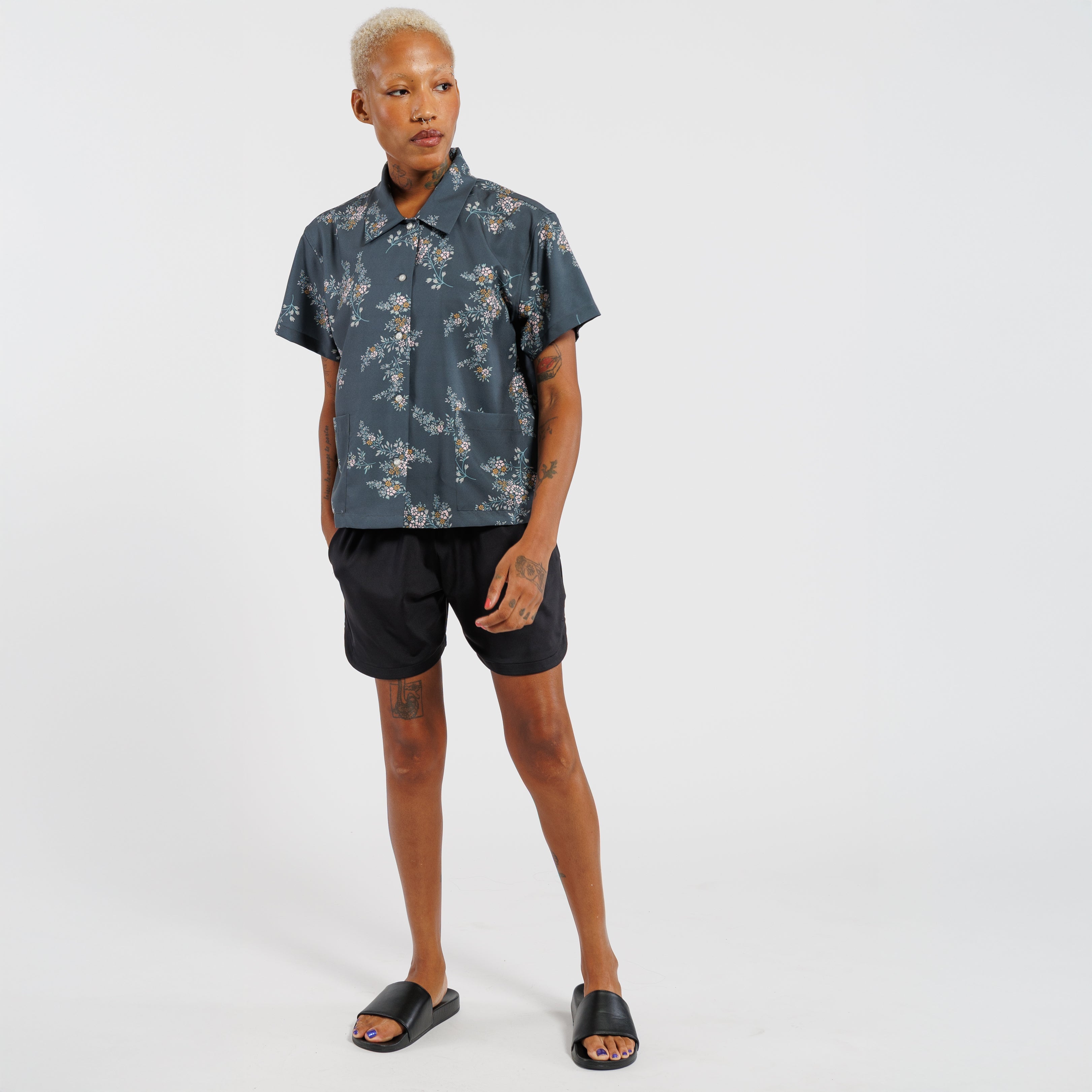 Person wearing a floral short-sleeve shirt and black shorts on a white background