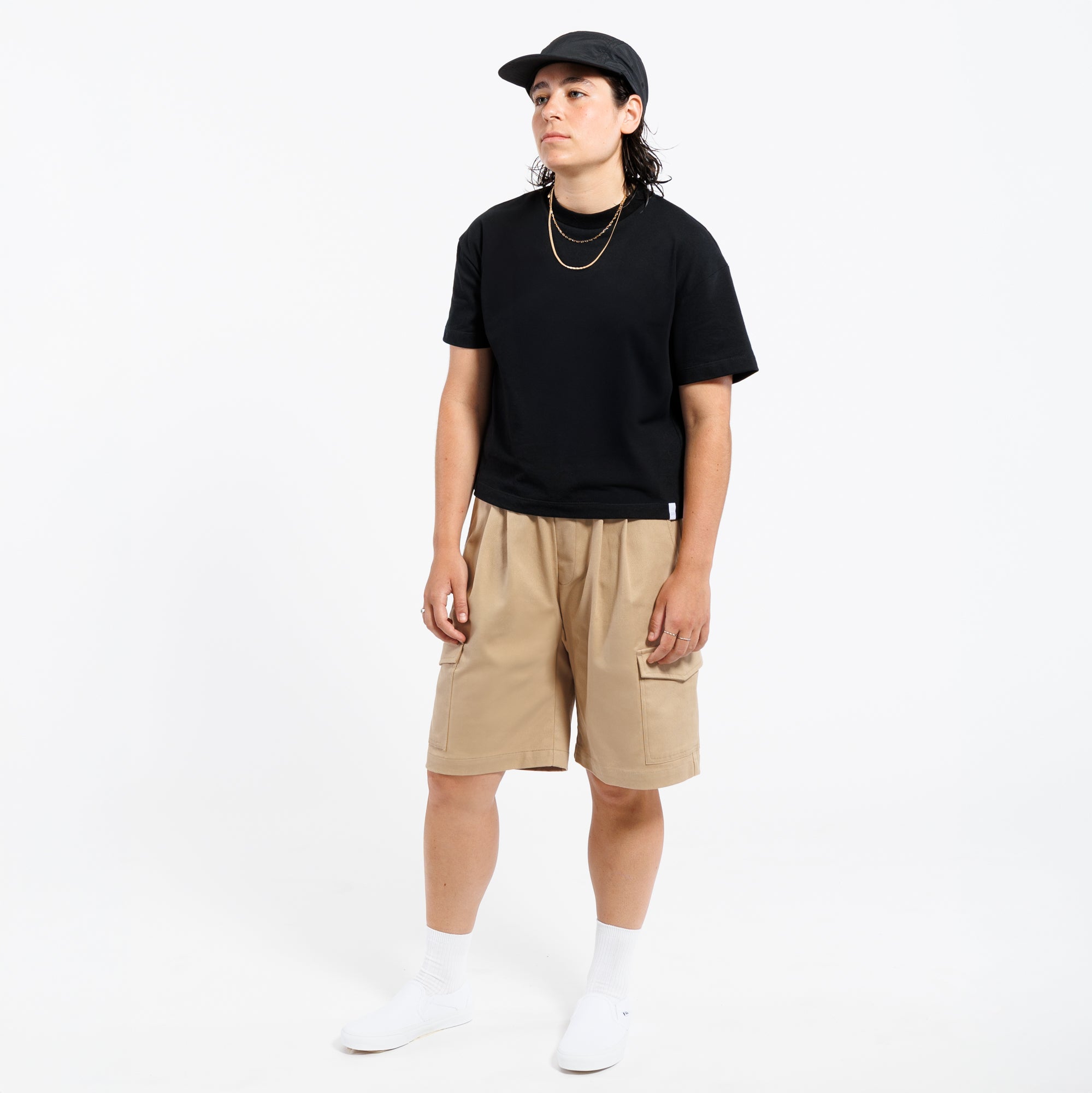 Person wearing a black t-shirt, khaki Bermuda shorts, and white sneakers on a white background