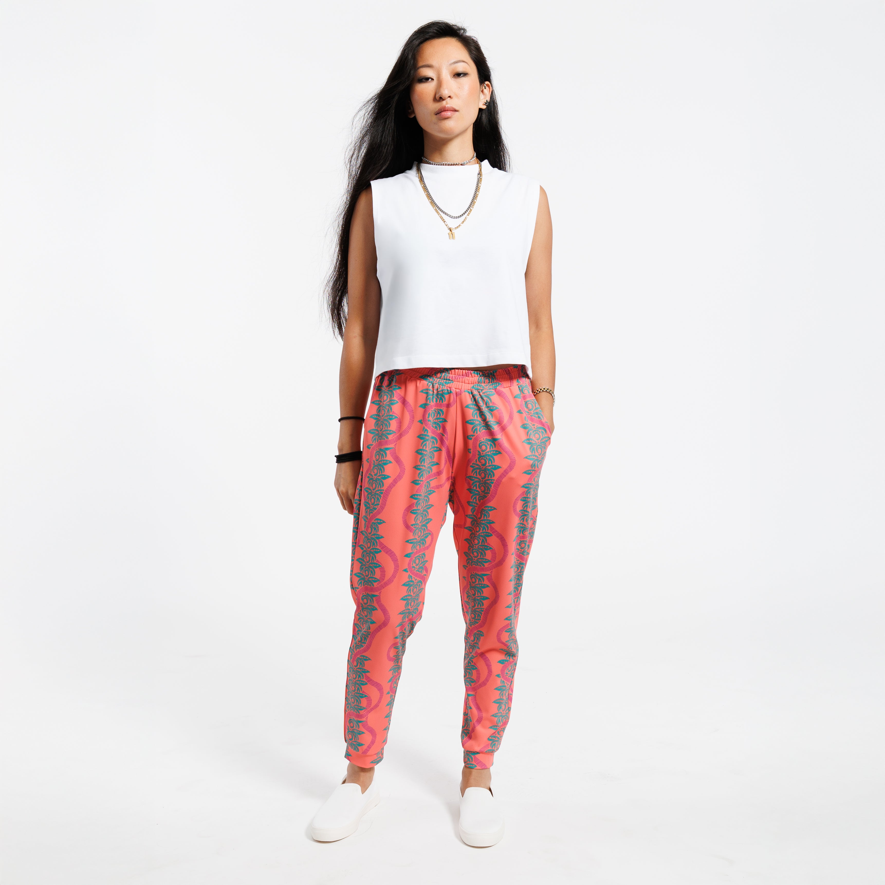 Woman wearing a white cropped tank top and pink patterned with green leaves pants on a white background
