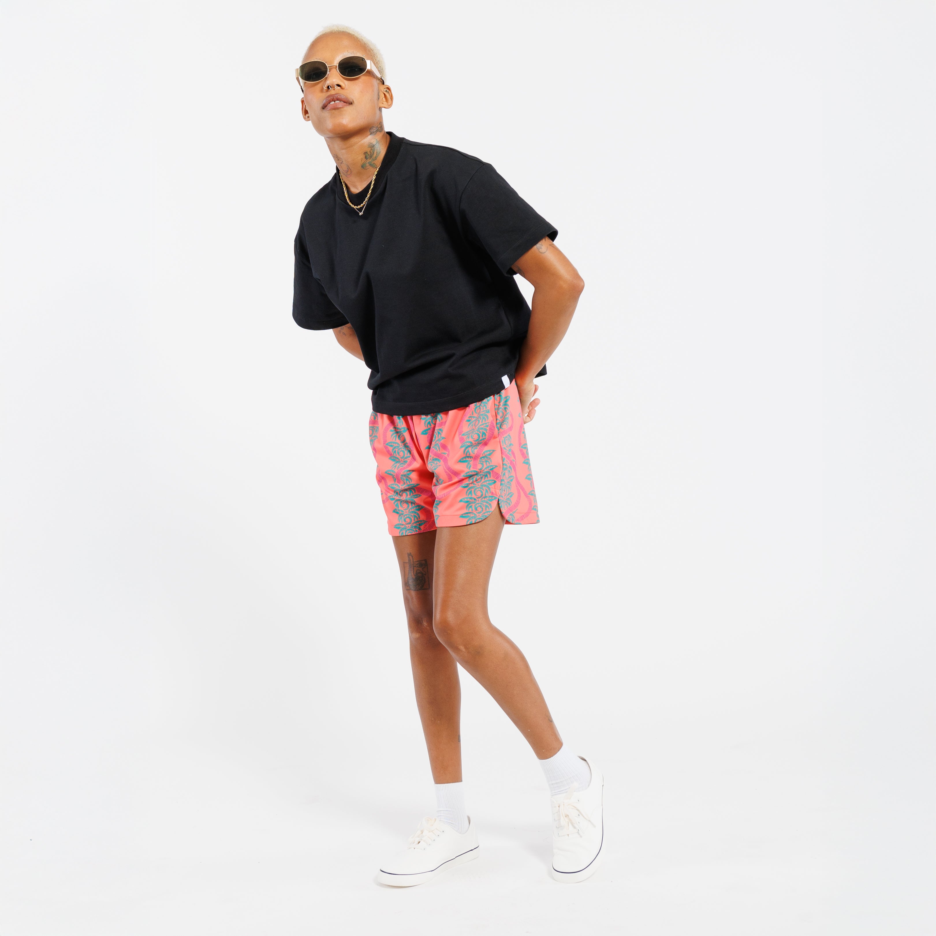 Person wearing a black oversized shirt and pink shorts with green leaf pattern on a white background