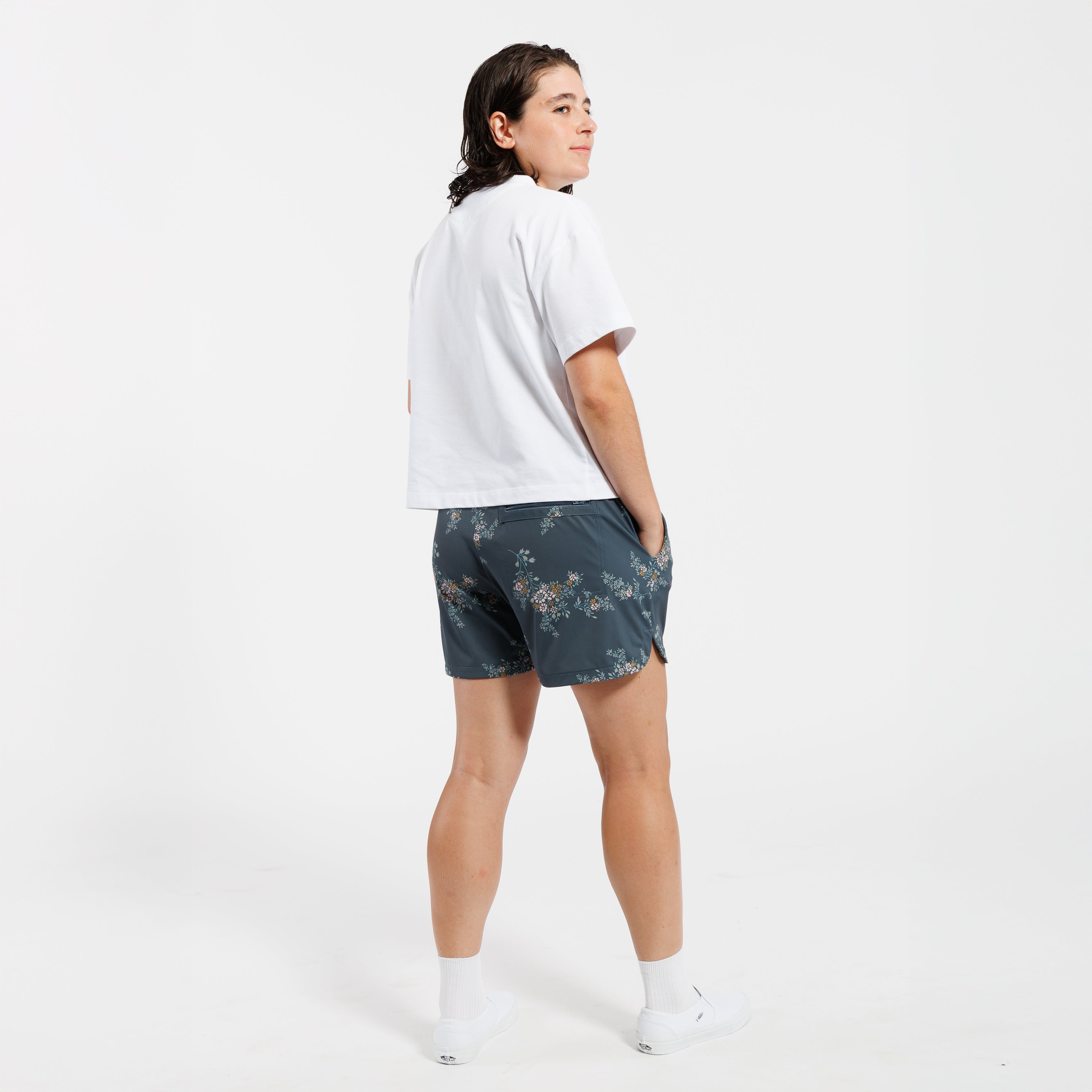 Person wearing a cropped white t-shirt and floral shorts on a white background