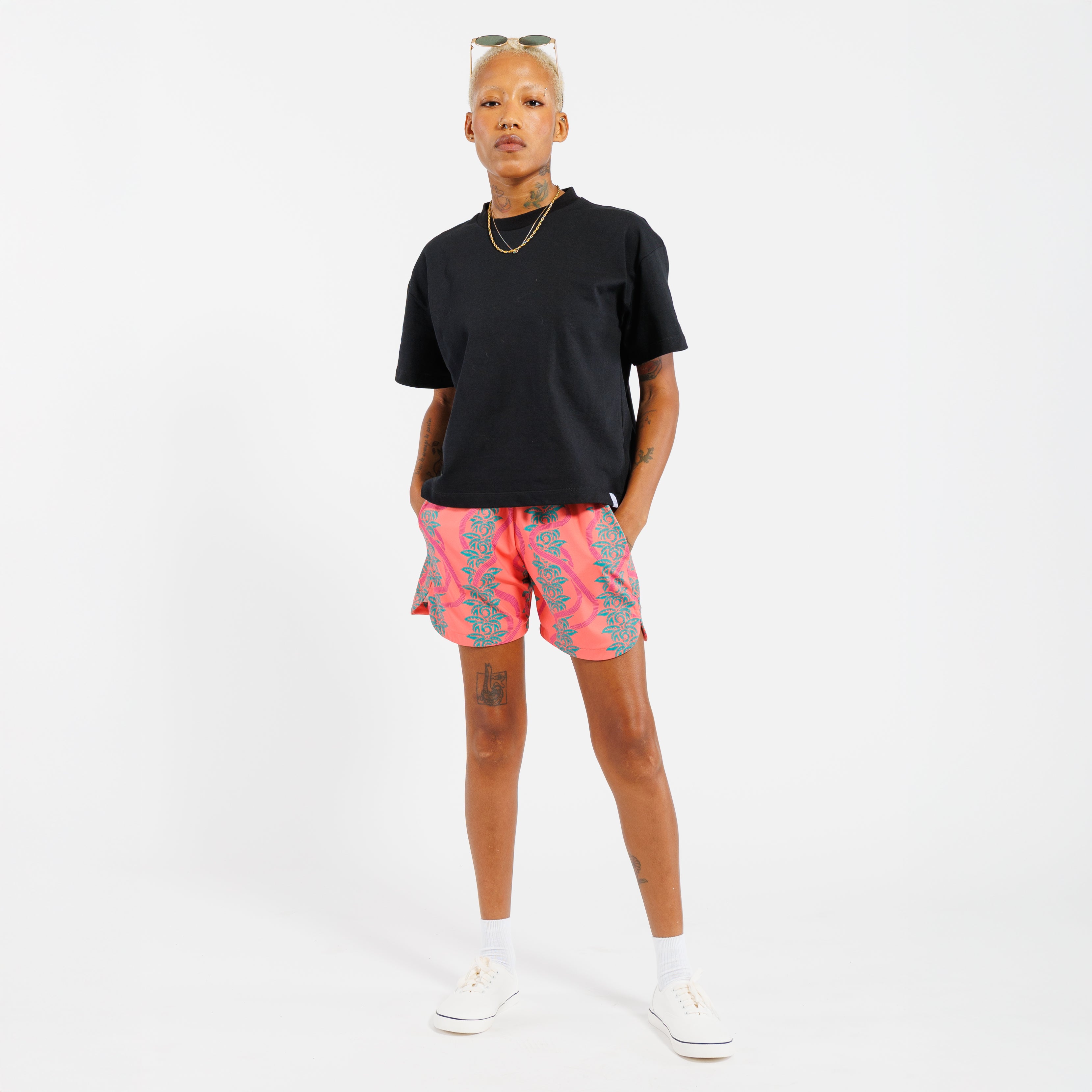 Person wearing a black t-shirt and pink shorts with green leaf pattern on a white background