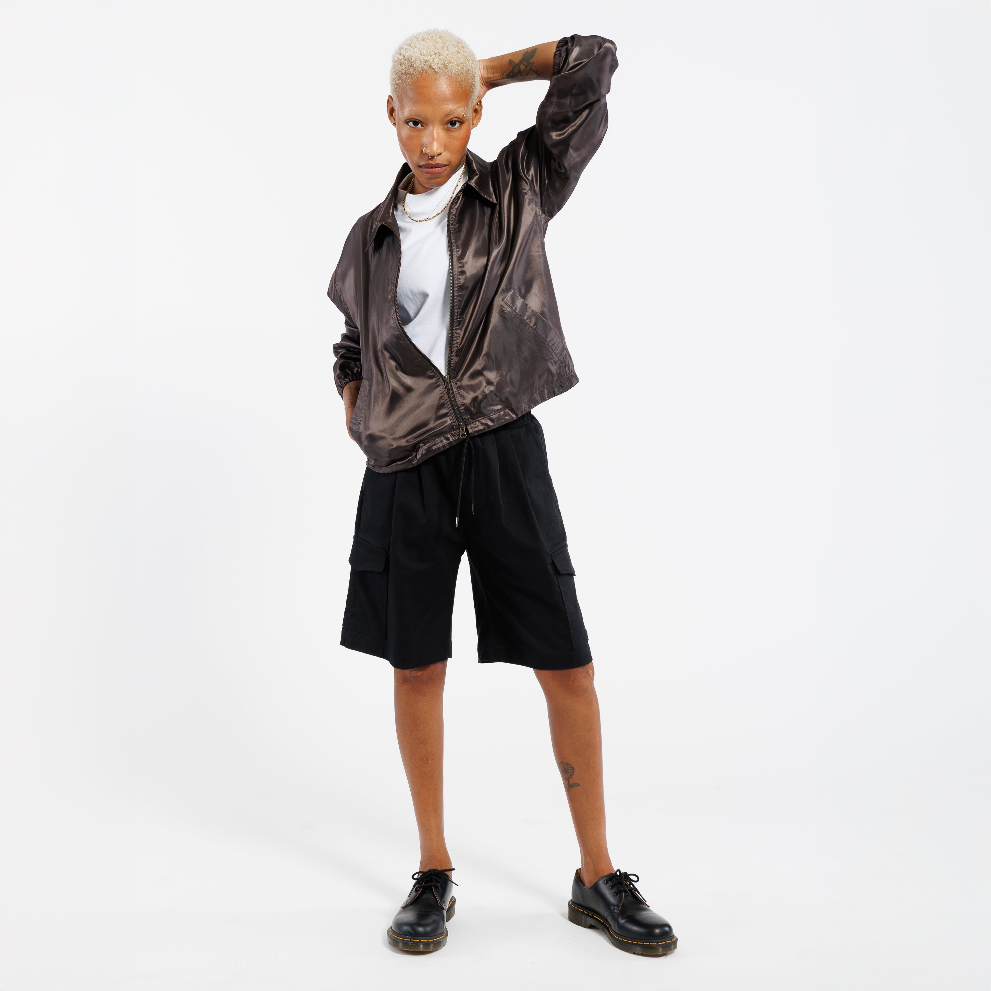 Person wearing a iridescent copper jacket, white shirt, black shorts, and black shoes on a white background