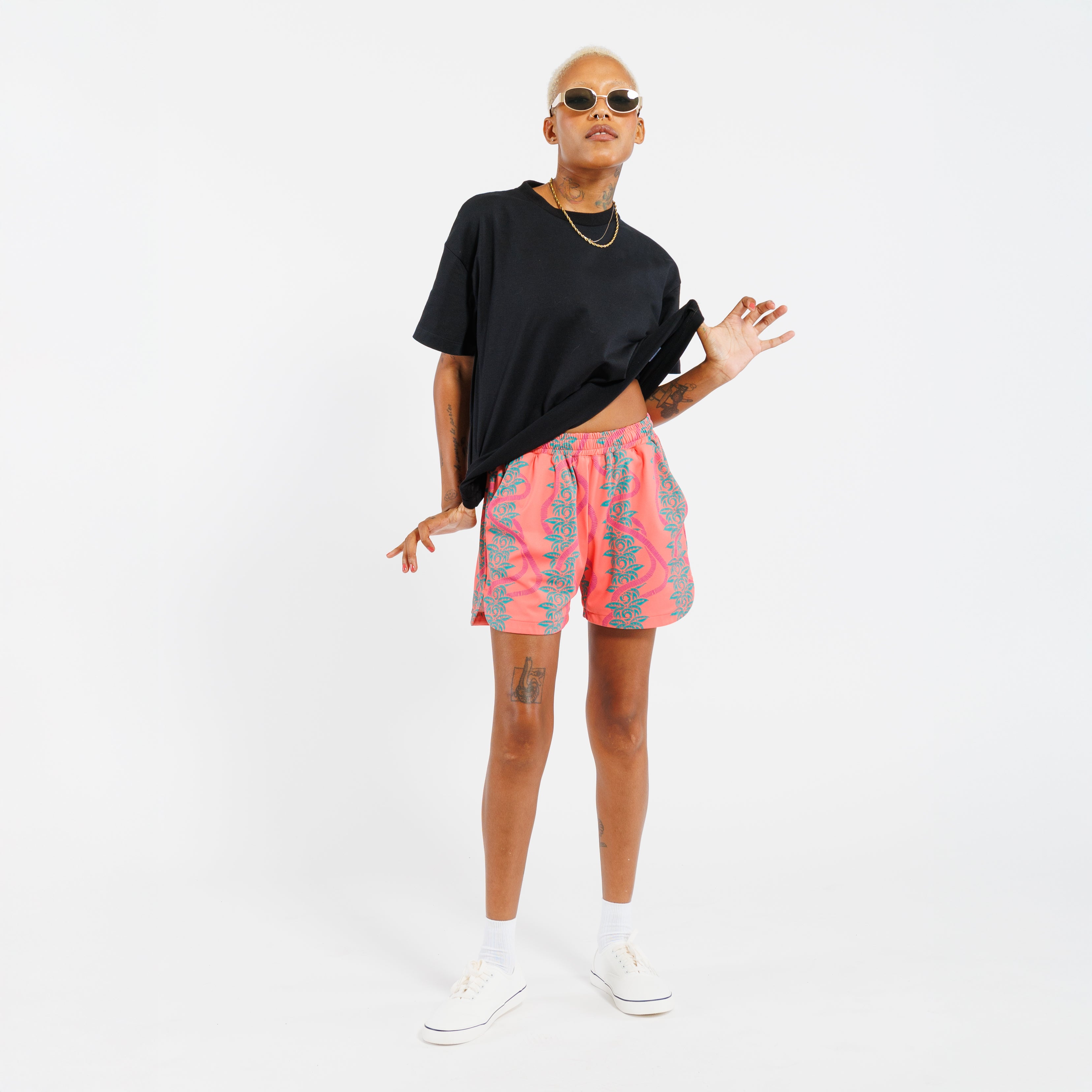 Person wearing a black t-shirt and pink shorts with green leaf pattern on a white background