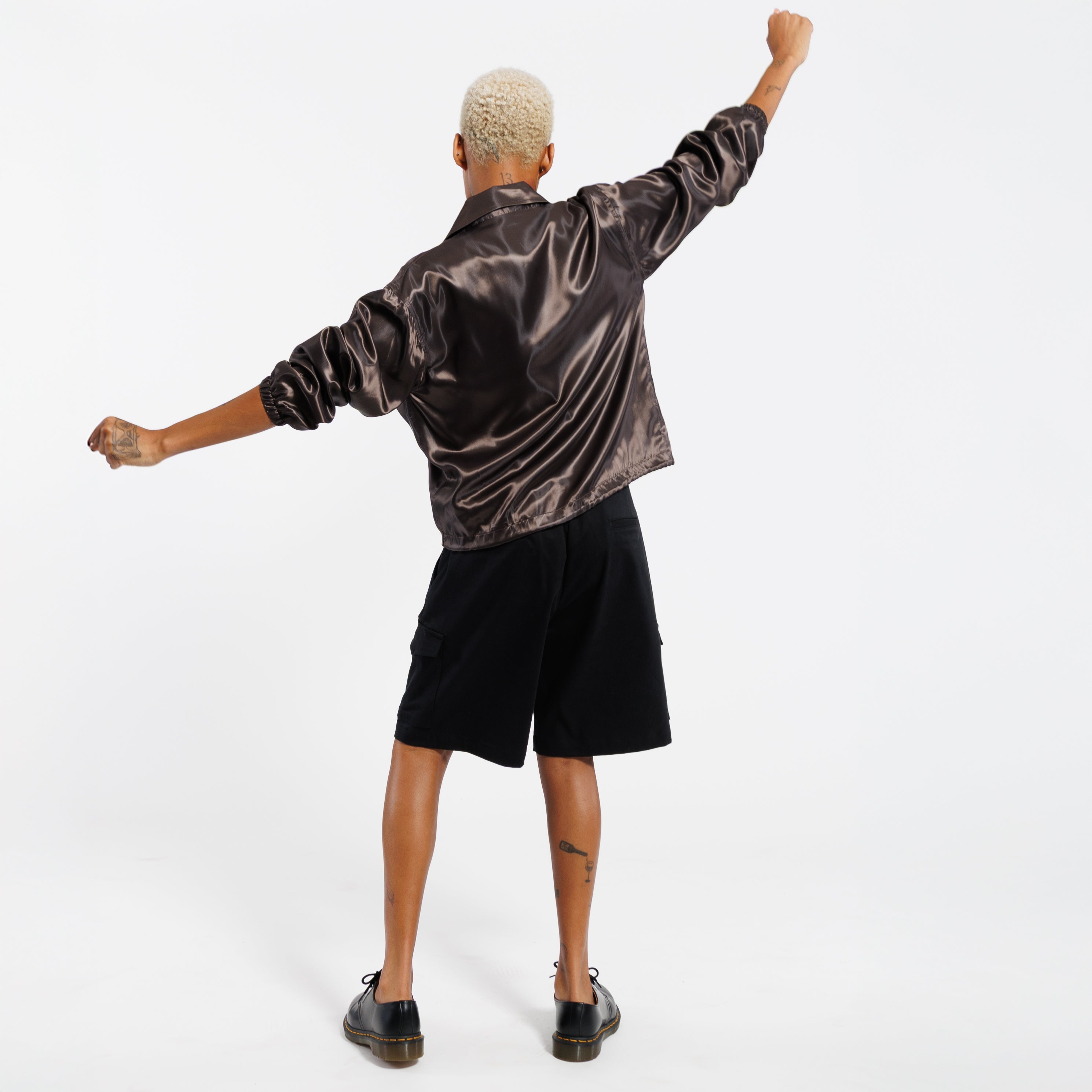 Person wearing a iridescent copper jacket, black shorts, and black shoes on a white background