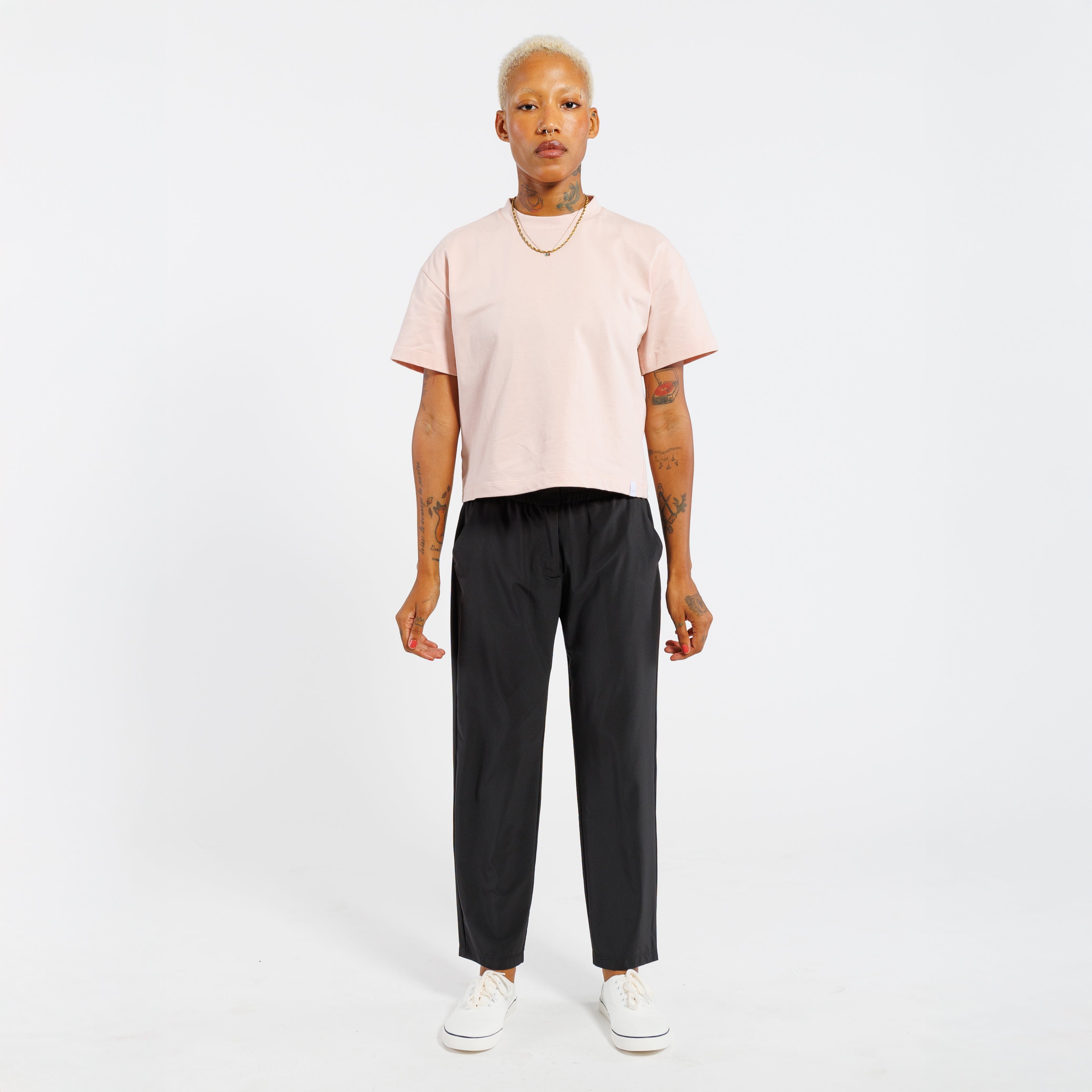 Person wearing a light pink t-shirt and black pants on a white background