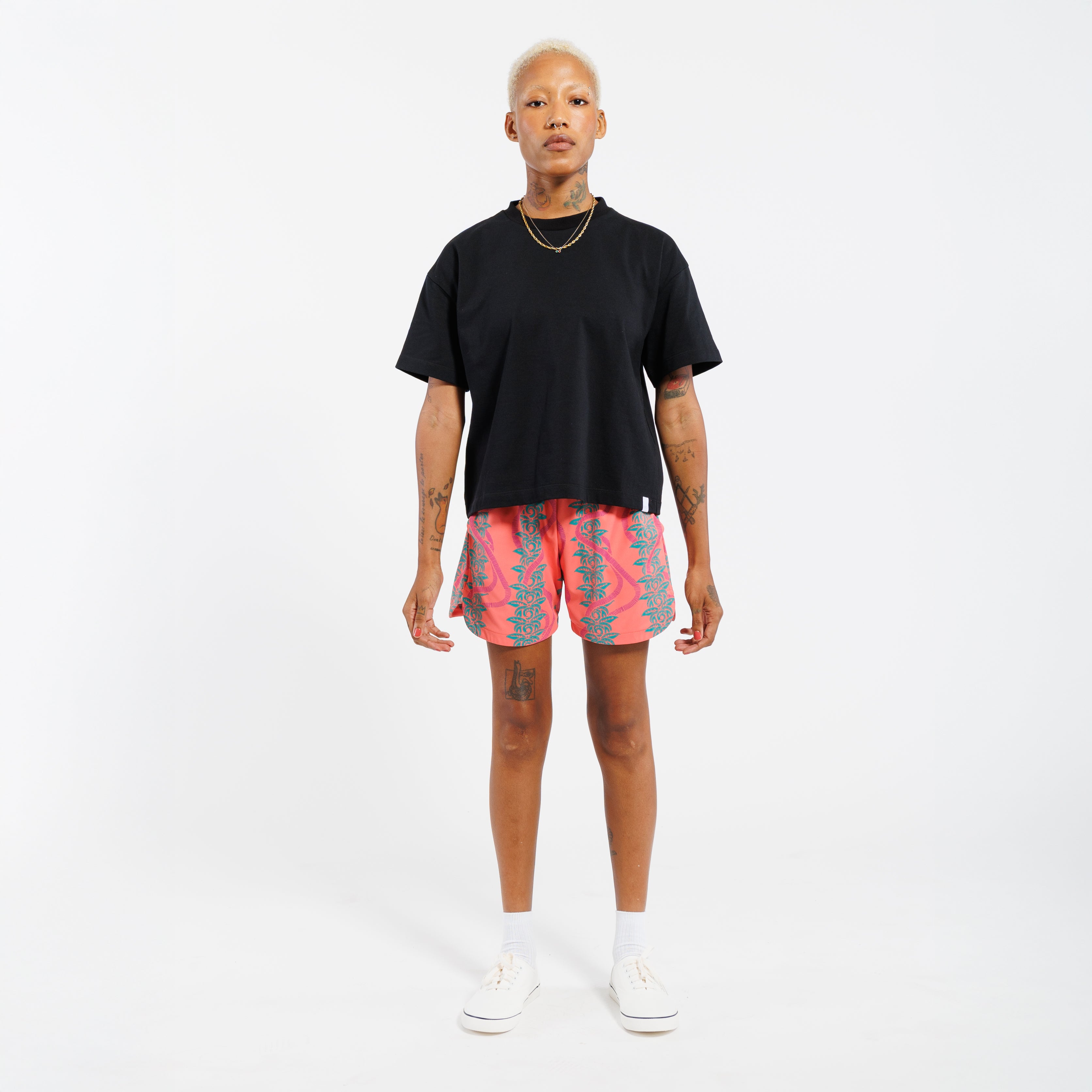Person wearing a black t-shirt and pink shorts with a green leaf pattern, standing in front of a white background
