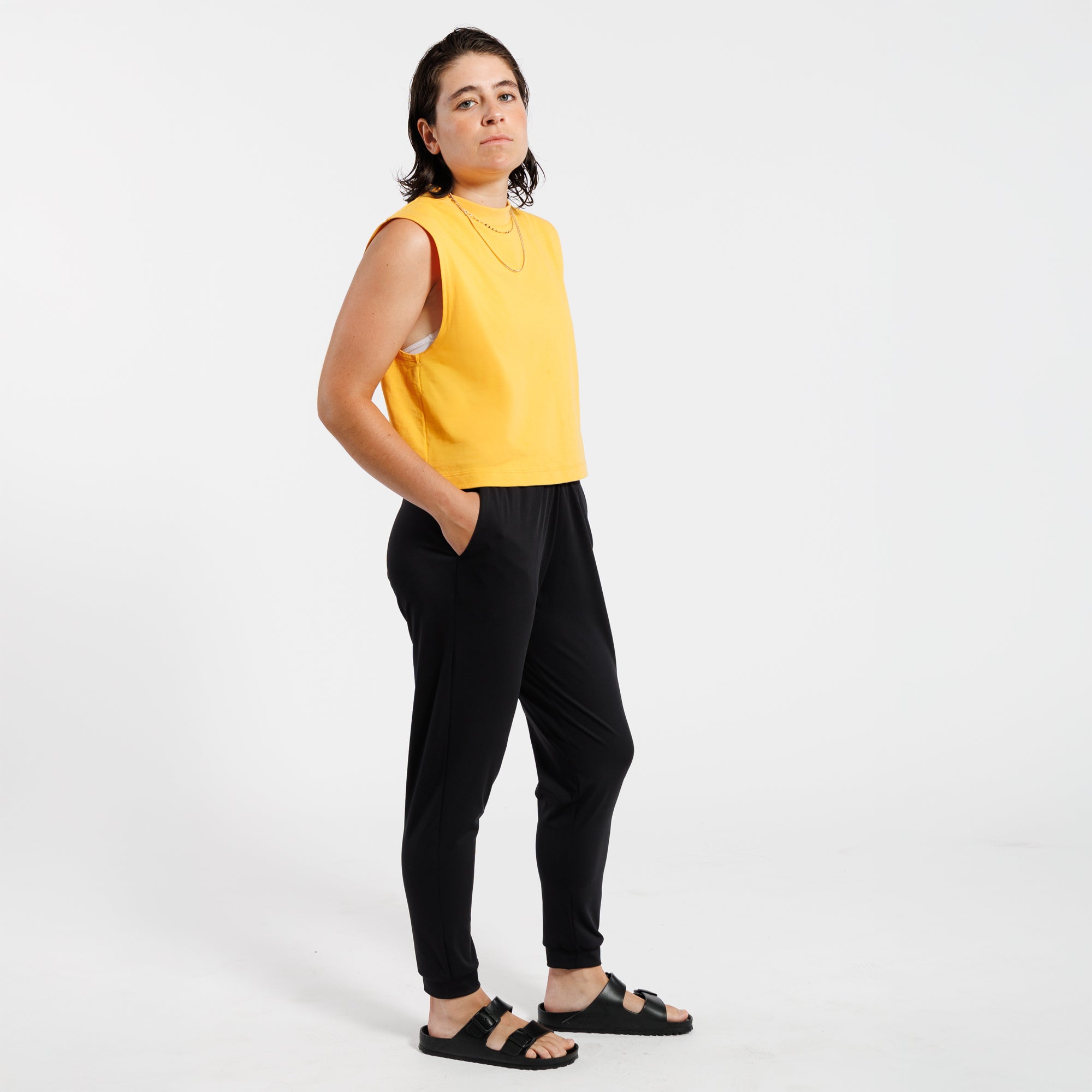 Person wearing a yellow sleeveless tank top and black pants on a white background