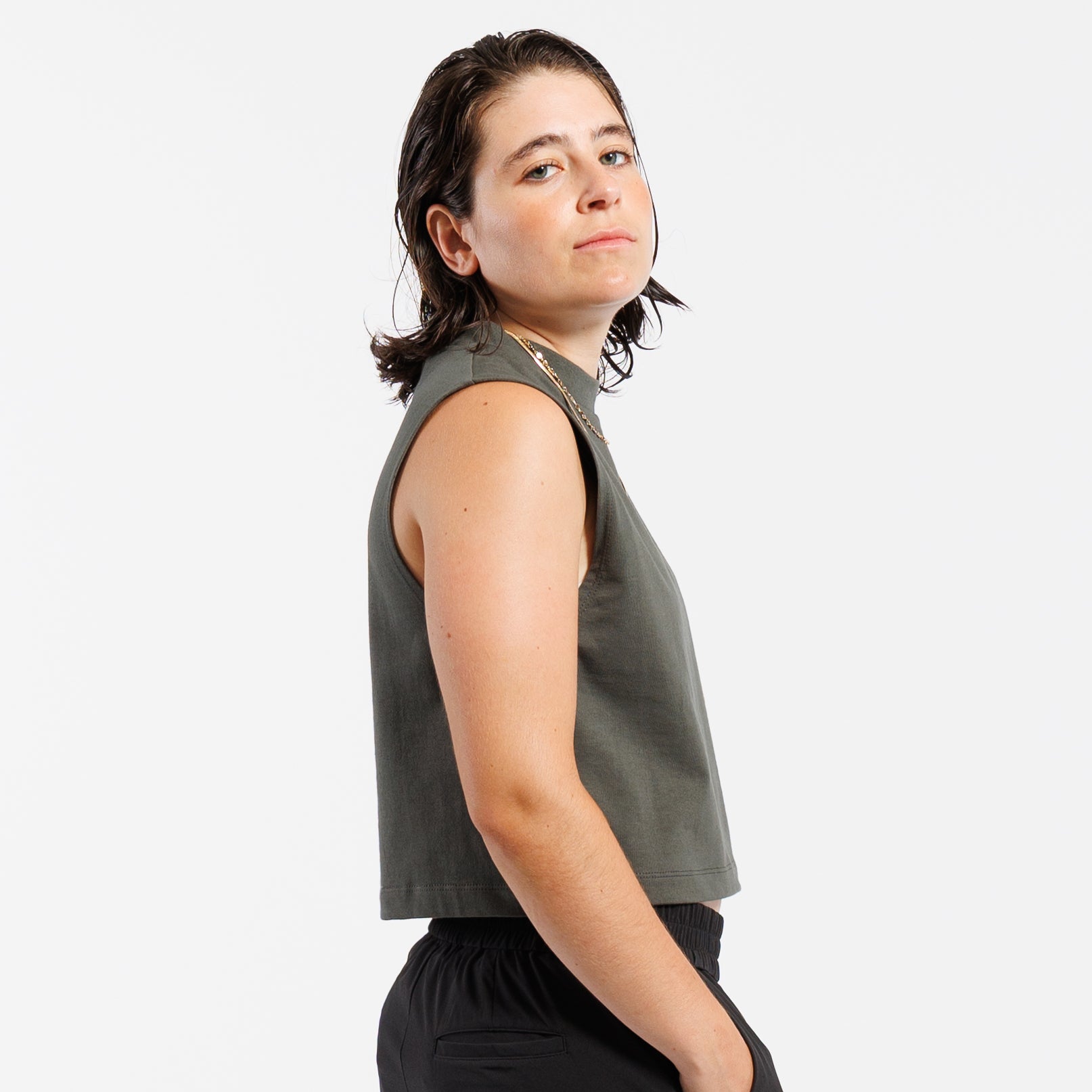 Person wearing gray cropped tank top and black pants on a white background