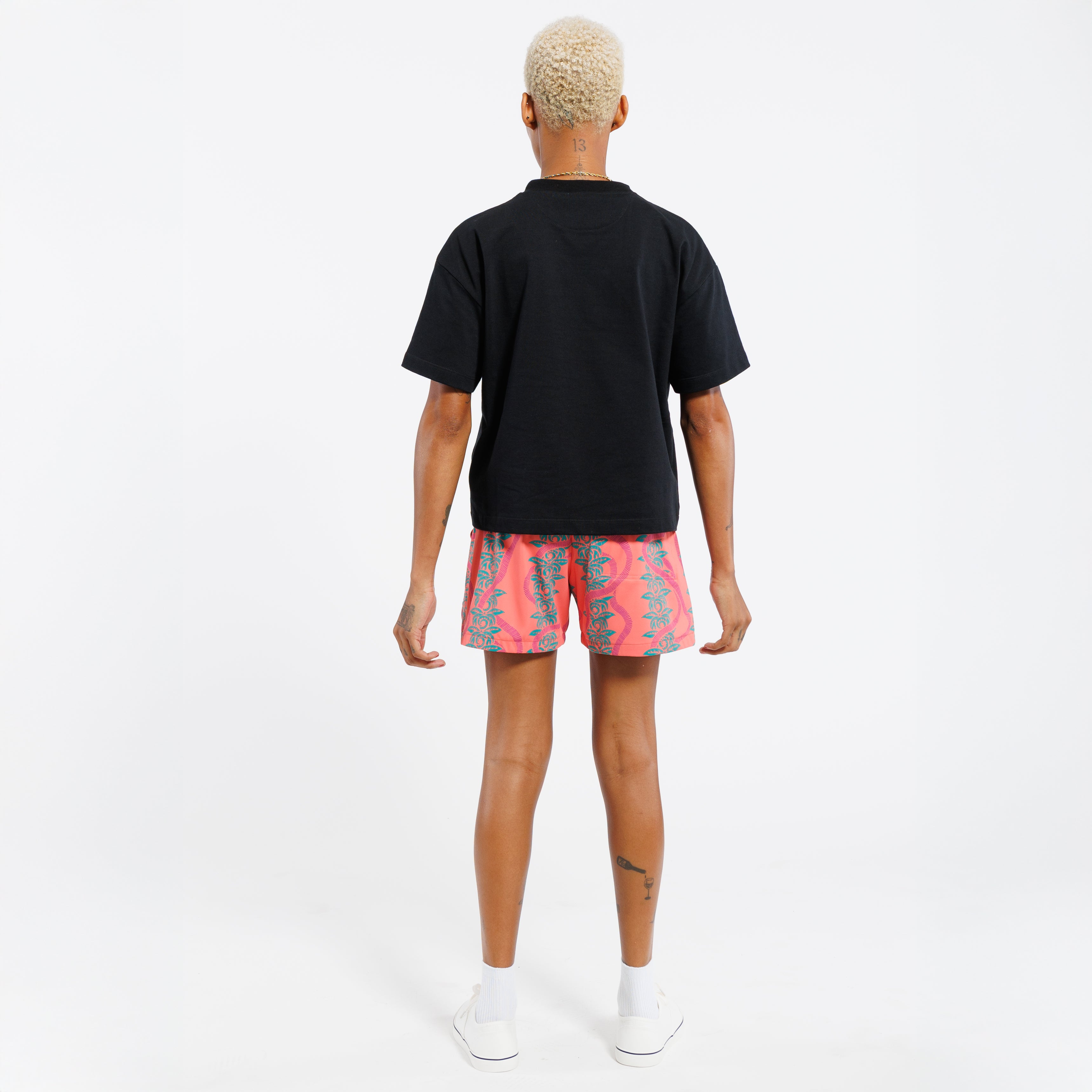 Person wearing a black t-shirt and pink shorts with green leaf pattern on a white background