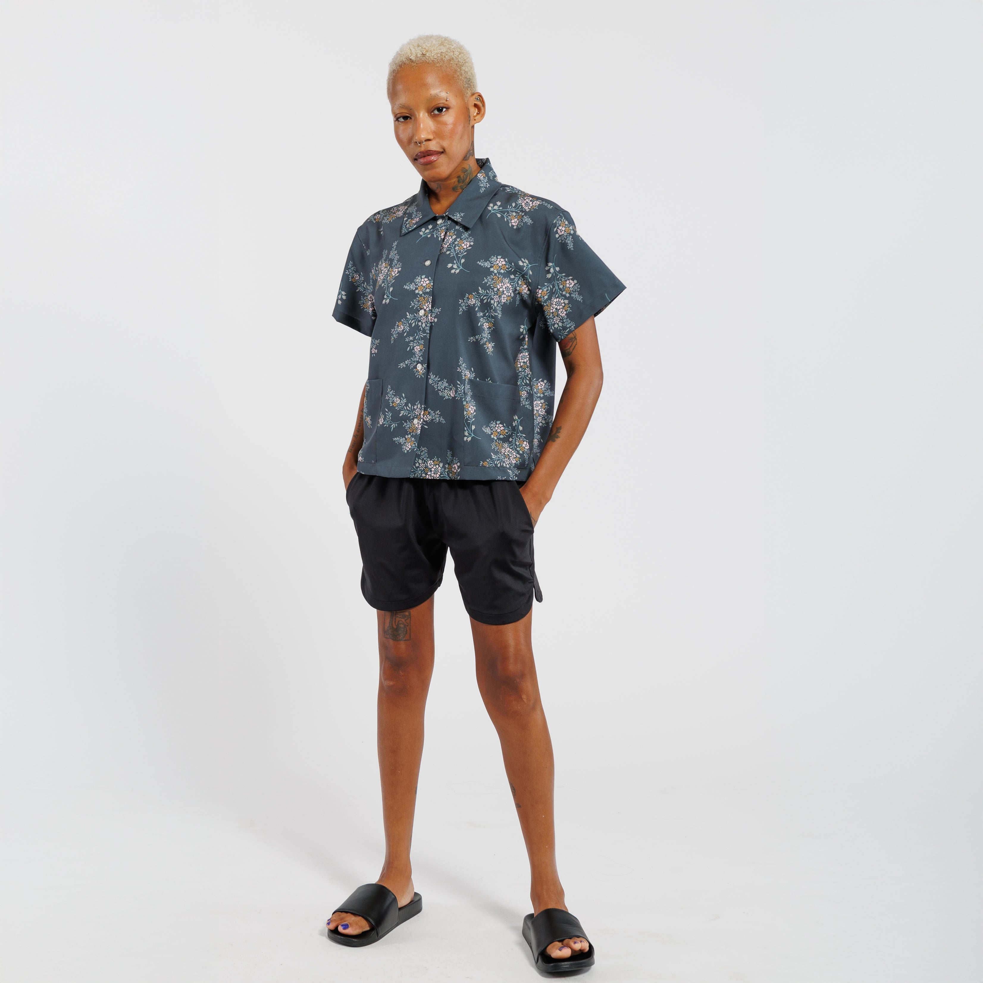 Person wearing a floral shirt and black shorts on a white background