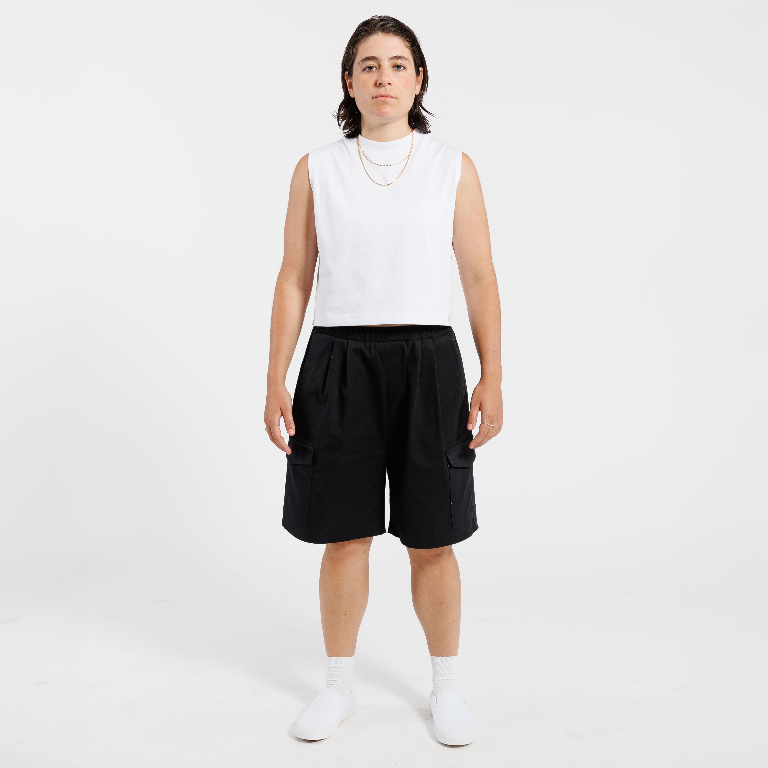 Person wearing a white tank top and black Bermuda shorts on a white background.