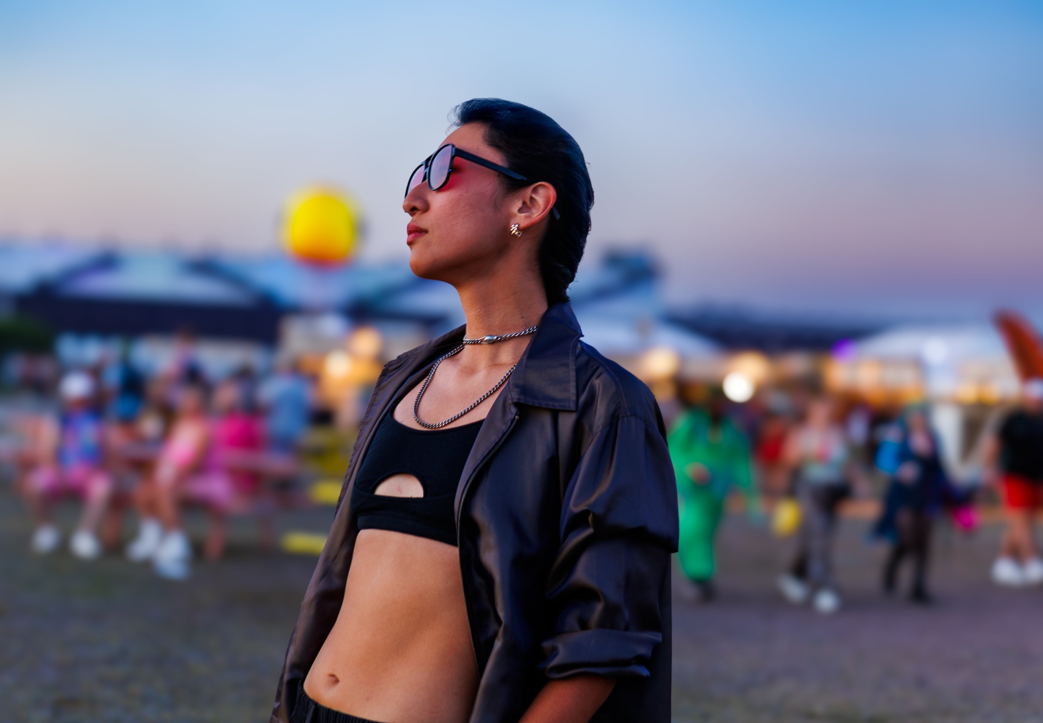 Woman wearing sunglasses and shiny purple jacket at a festival with blurred background