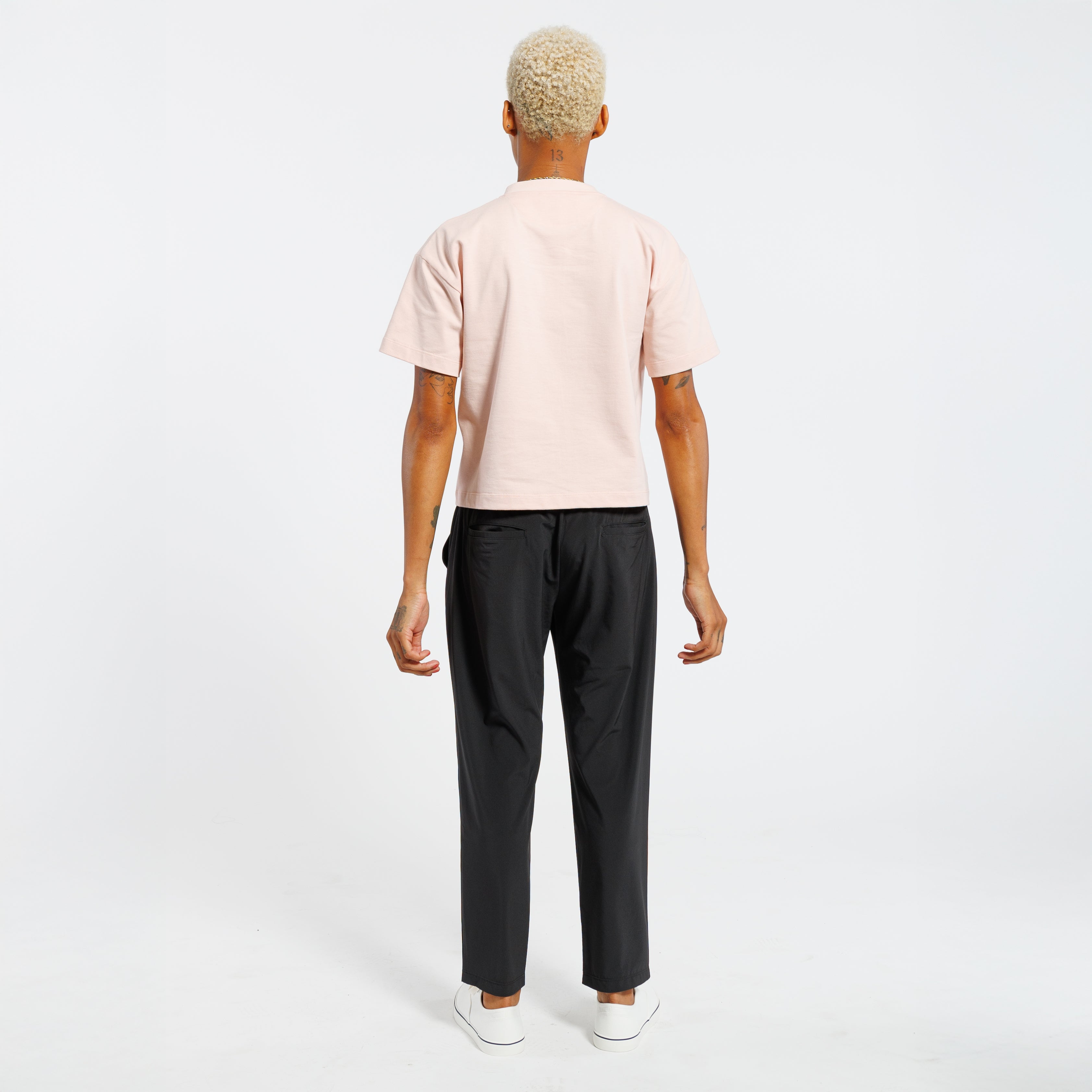 Back view of a person wearing a light pink t-shirt and black pants on a white background
