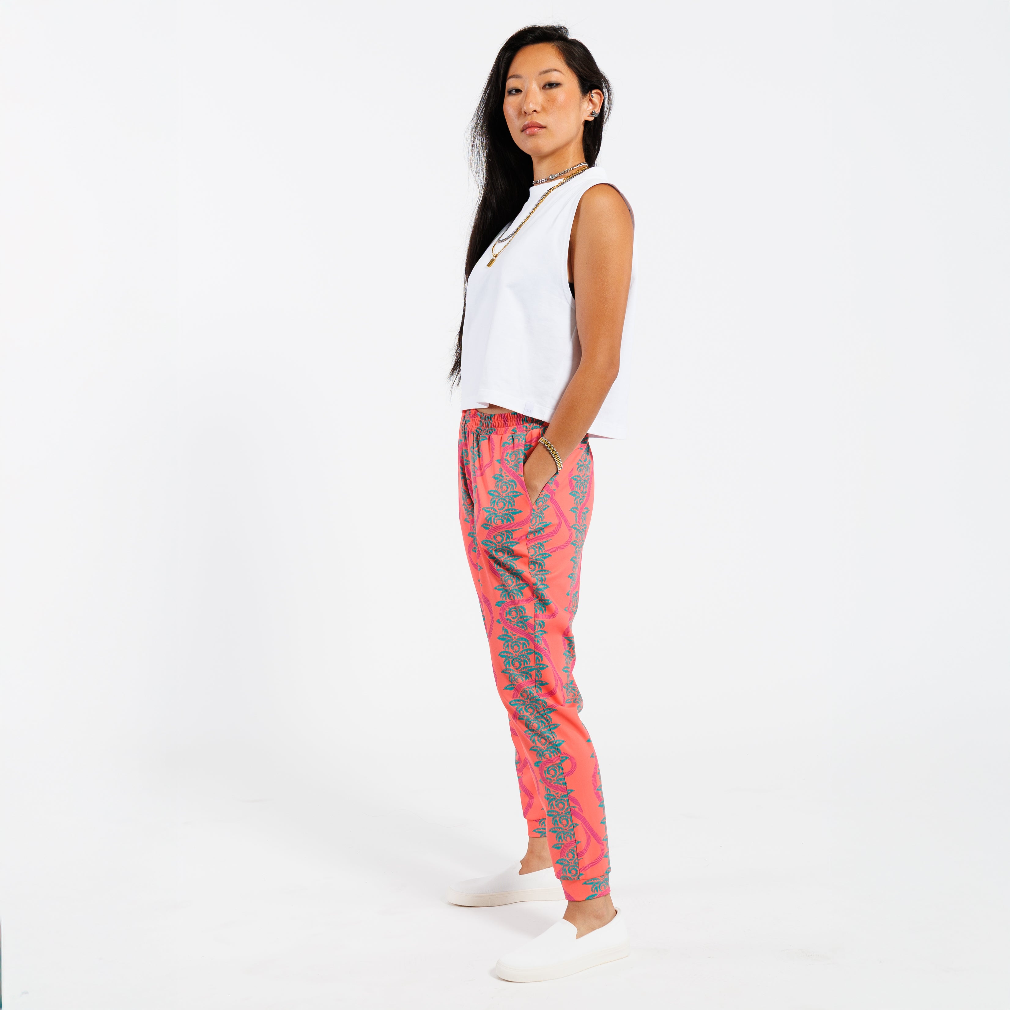 Woman wearing a white cropped tank top and pink patterned with green leaves pants on a white background