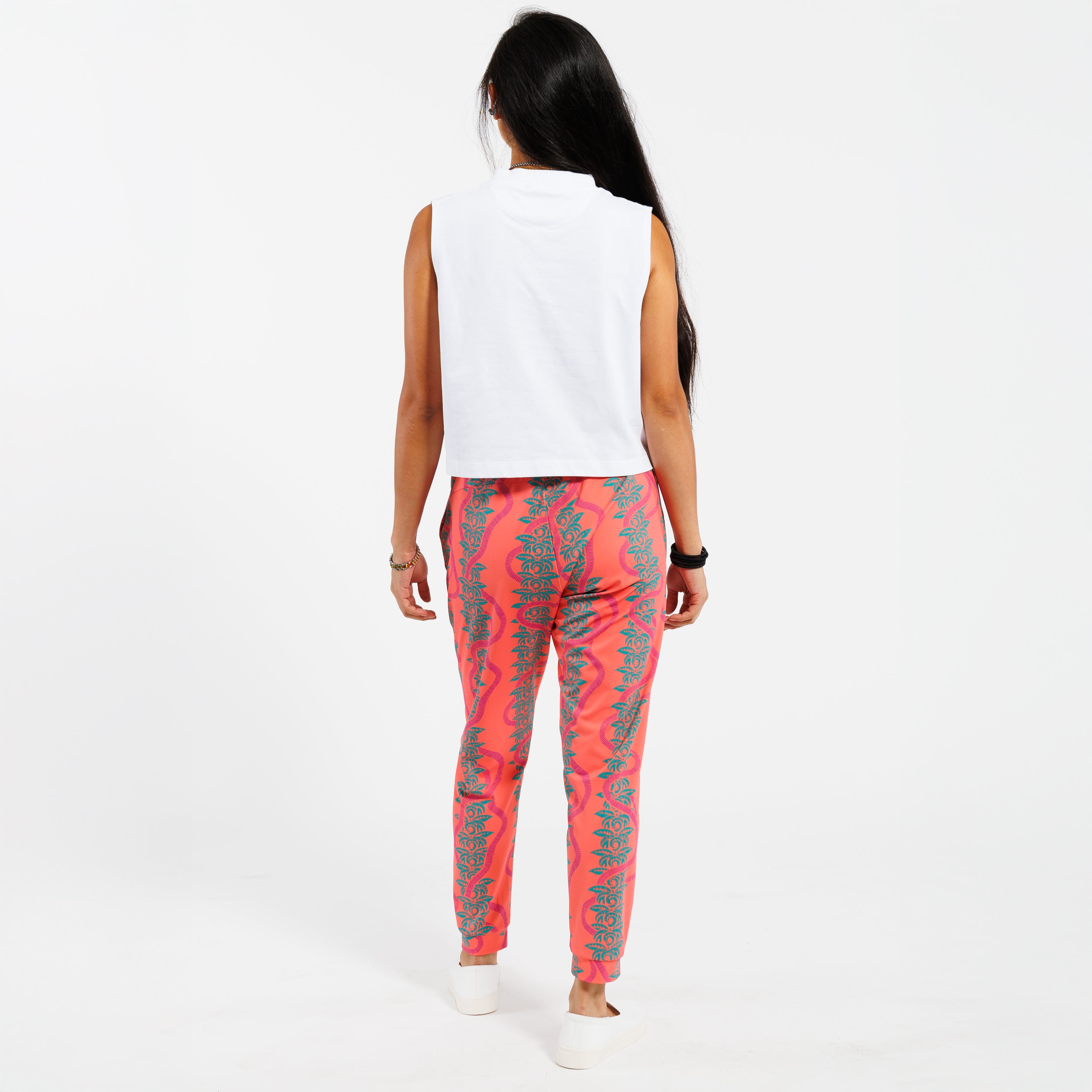 Woman wearing a white cropped tank top and pink patterned with green leaves pants on a white background