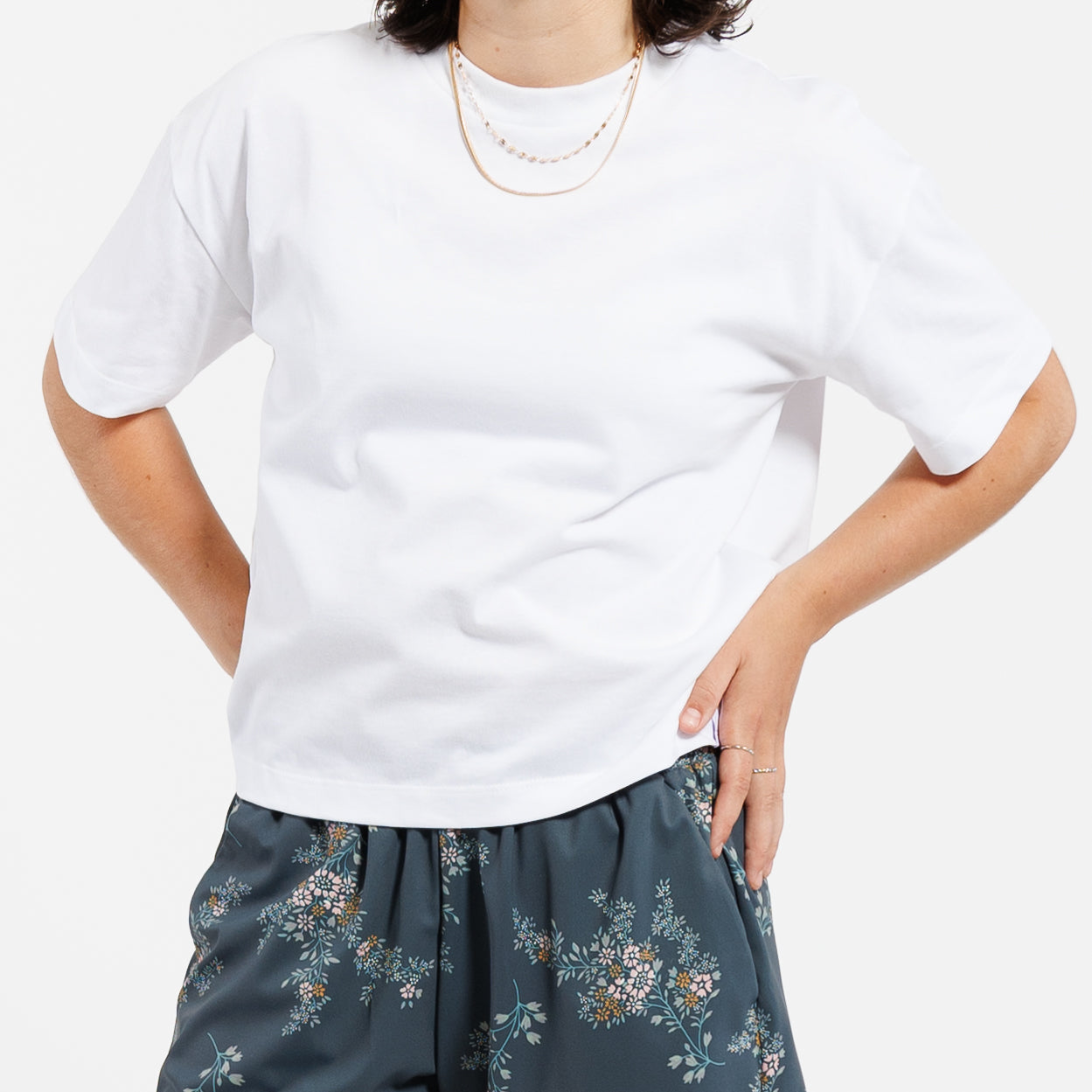Person wearing a cropped white t-shirt and floral bottoms on a white background