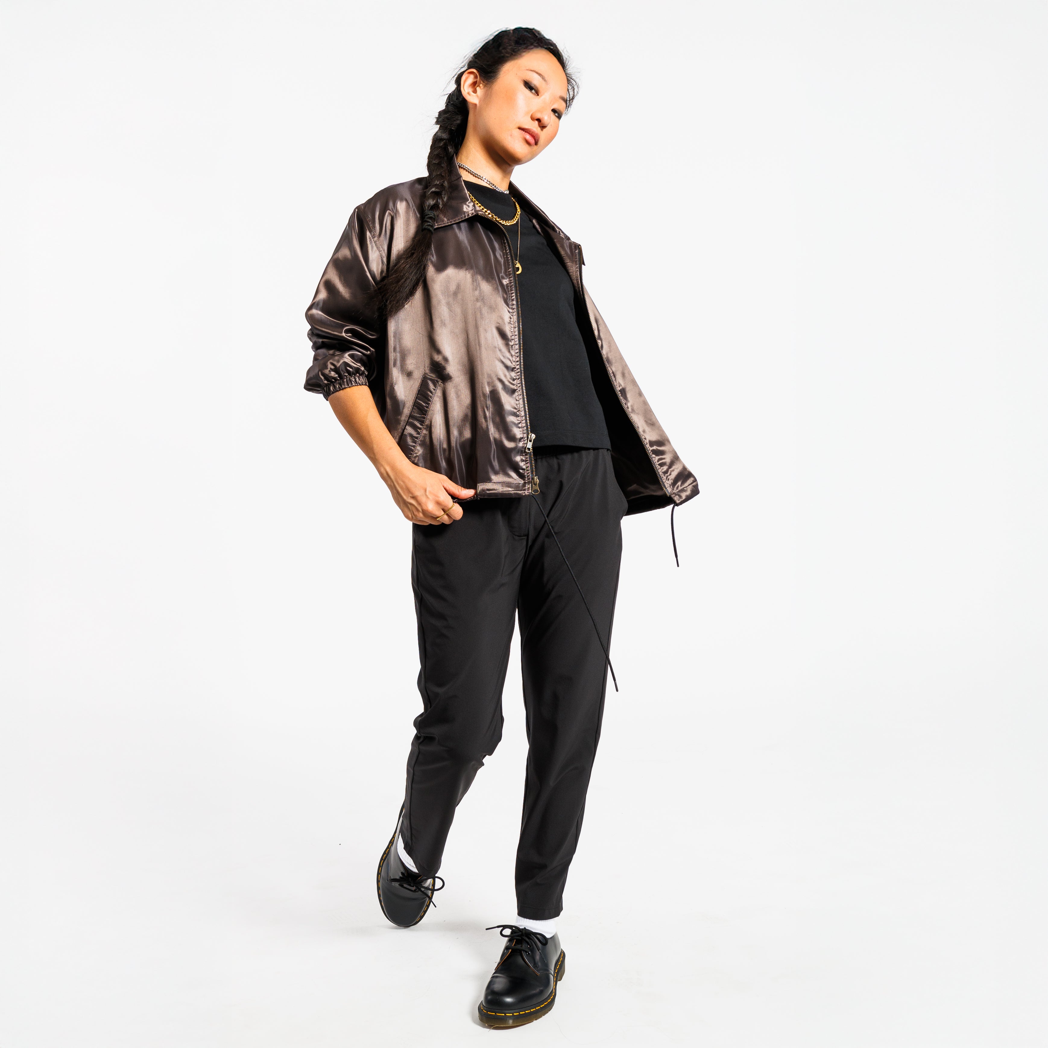 Person wearing a shiny copper jacket and black pants on a white background