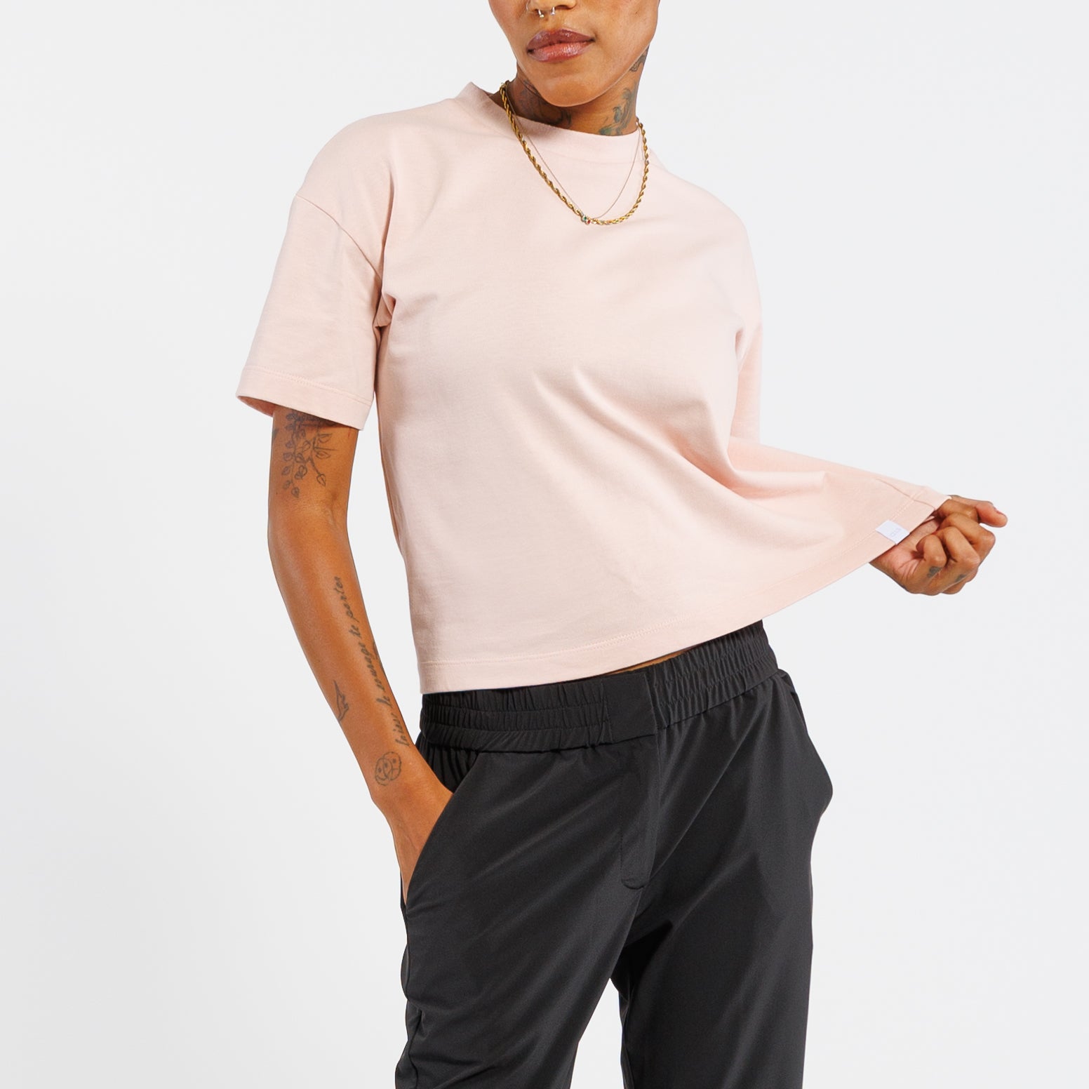 Person wearing a light pink t-shirt and black pants on a white background