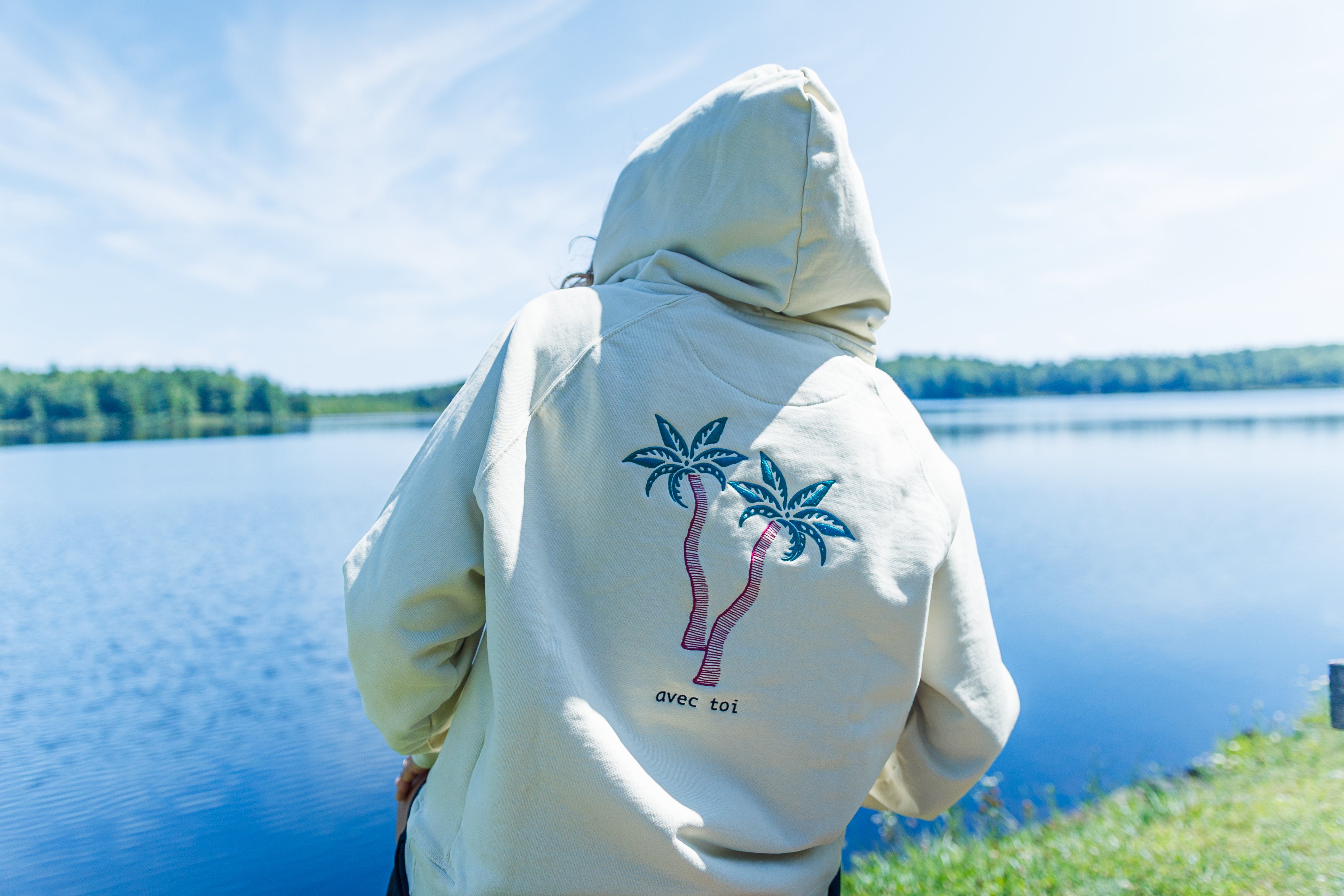 Person wearing a hoodie with palm tree design by a lake.