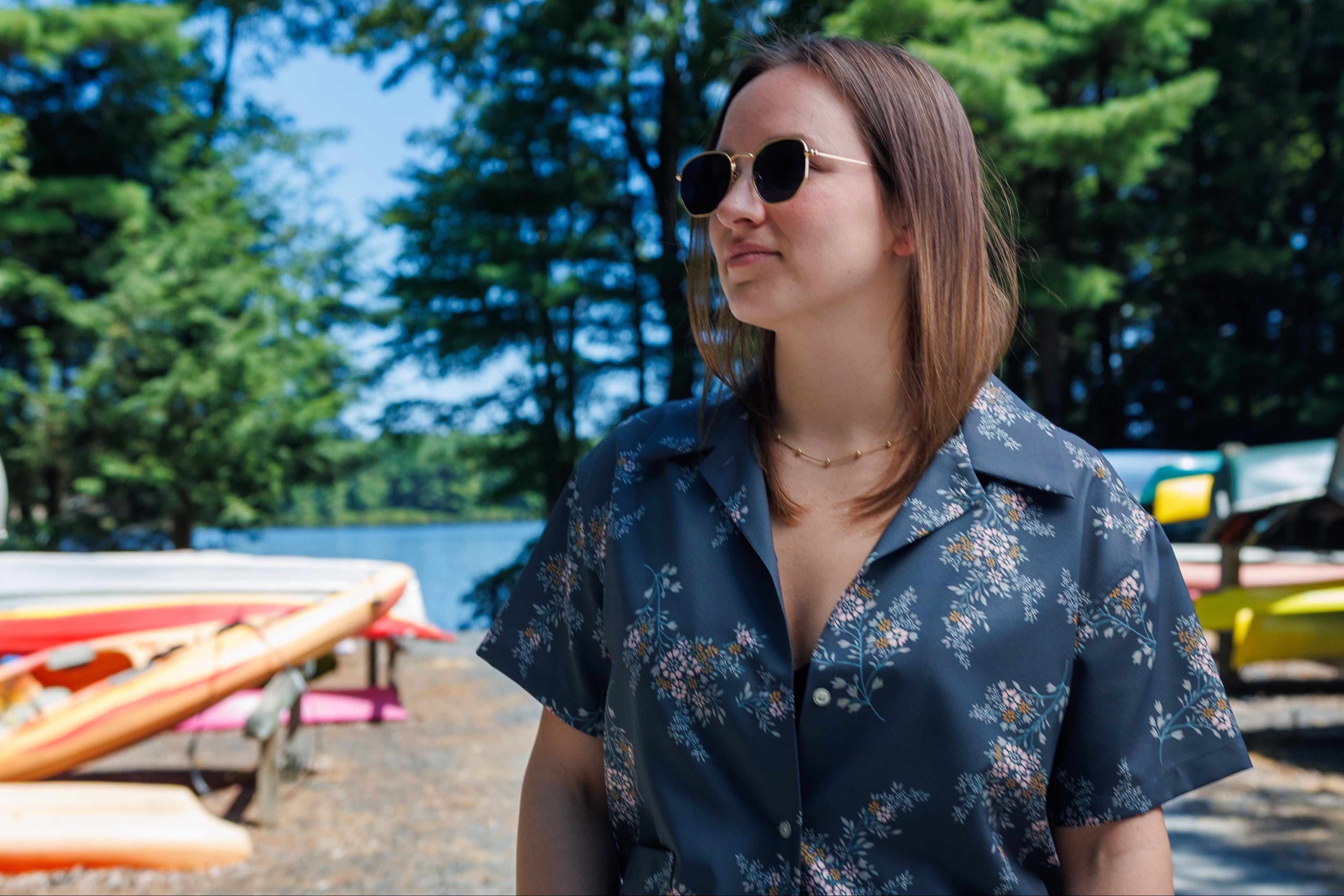 Woman wearing a floral button-down shirt standing in a forested boatyard.