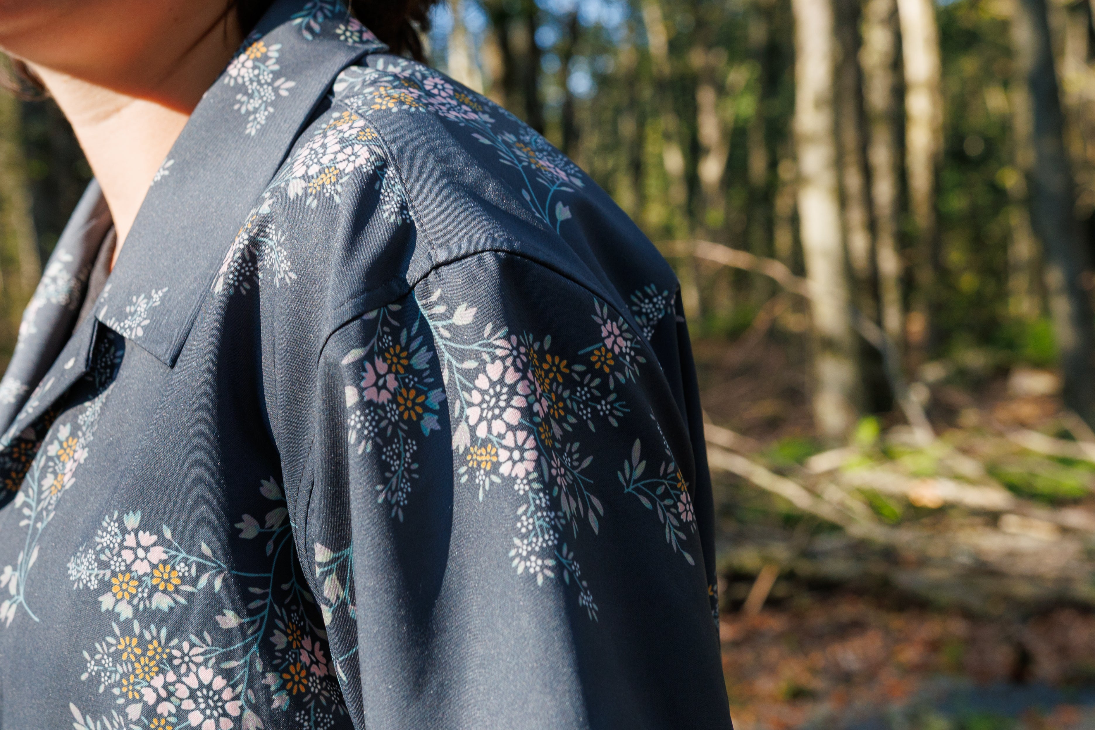 Person in a floral button-down shirt, highlighting collar and sleeve details, standing in a forest setting.