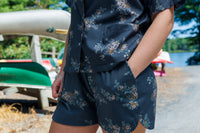 Floral shirt and shorts set displayed in a forested boatyard.