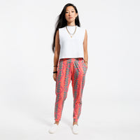Woman wearing a white cropped tank top and pink patterned with green leaves pants on a white background