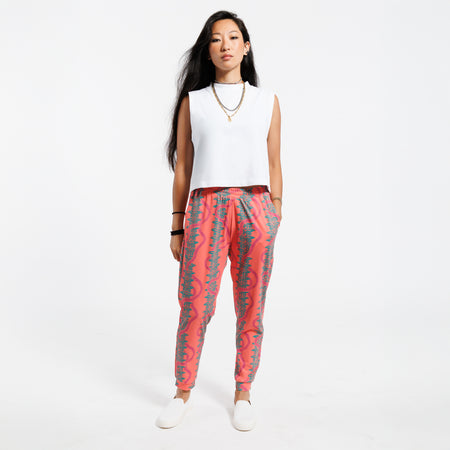 Woman wearing a white cropped tank top and pink patterned with green leaves pants on a white background