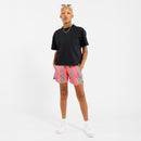 Person wearing a black t-shirt and pink shorts with green leaf pattern on a white background 