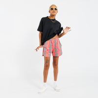 Person wearing a black t-shirt and pink shorts with green leaf pattern on a white background 