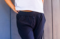 Person wearing black pants and a white top against a wooden wall.