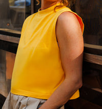 Person wearing a yellow sleeveless top standing next to a reflective surface.