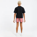 Back view of a person wearing a black t-shirt and pink shorts with a green leaf pattern, standing in front of a white background