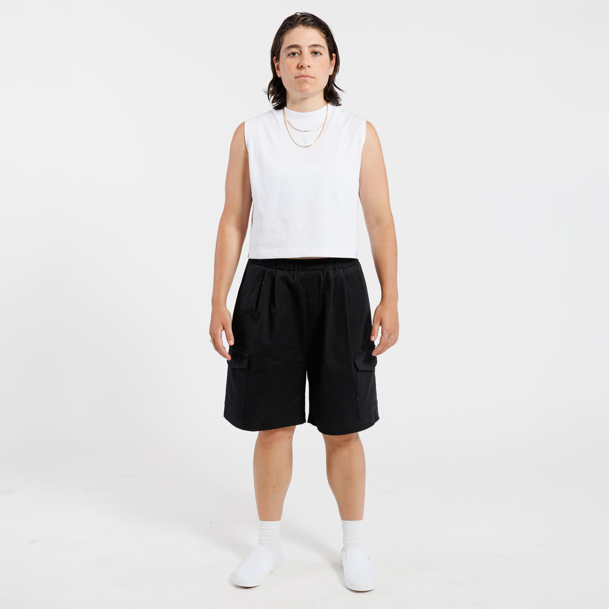 Person wearing a white tank top and black Bermuda shorts on a white background.