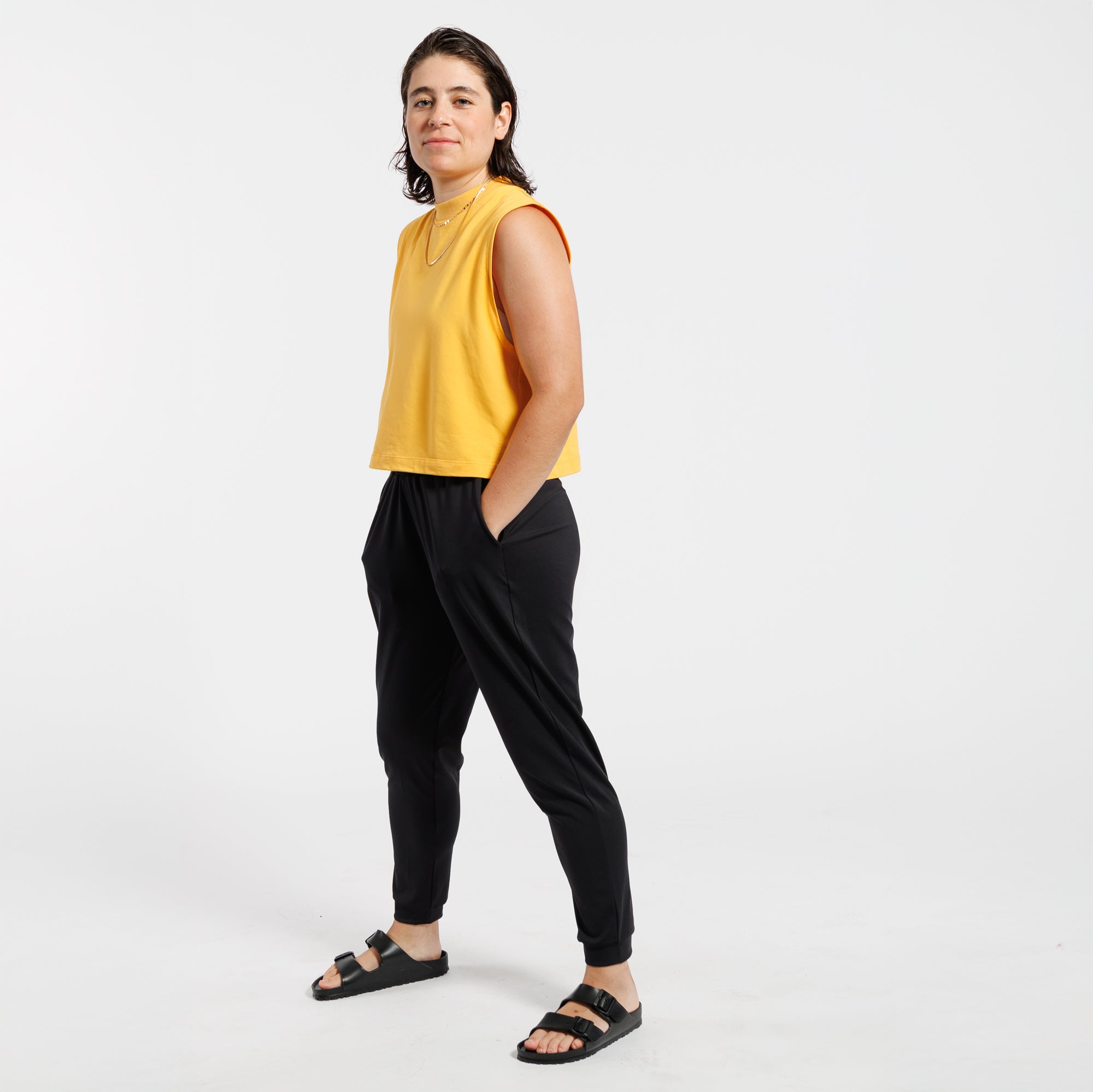 Woman wearing a yellow sleeveless tank top and black pants on a white background