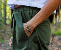 Close-up of olive green Bermuda shorts showing pocket detail with a woman’s hand inside the pocket.