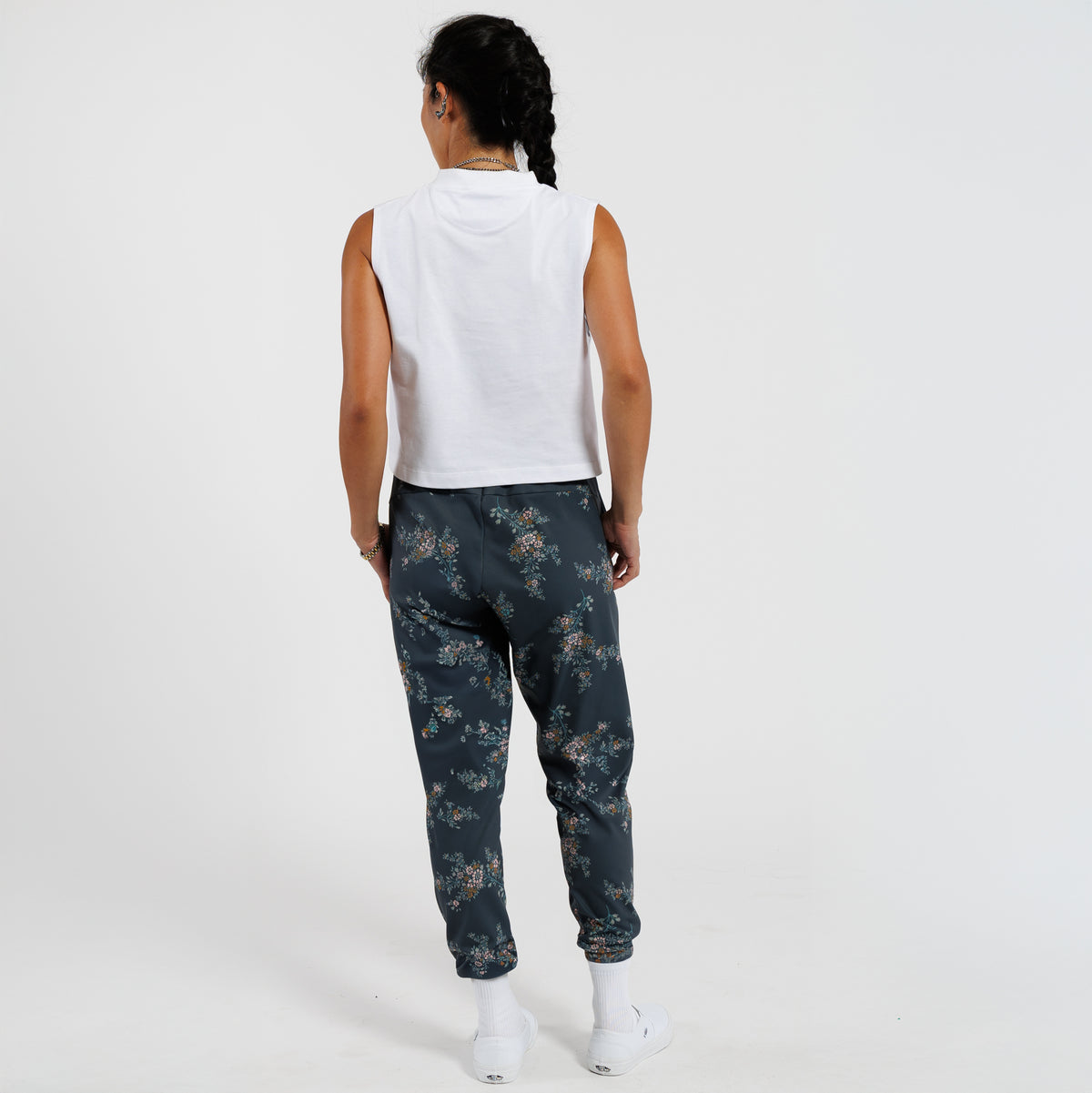 Person wearing a white sleeveless top and dark floral pants on a white background