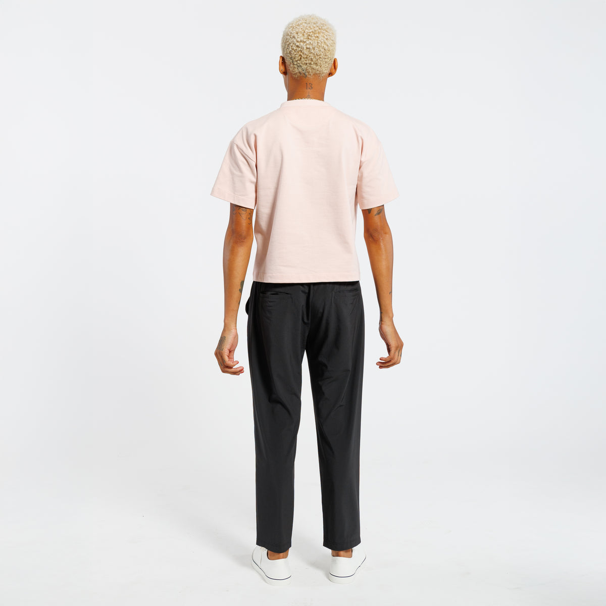 Back view of a person wearing a light pink t-shirt and black pants on a white background