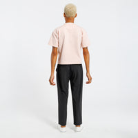Back view of a person wearing a light pink t-shirt and black pants on a white background