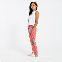 Woman wearing a white cropped tank top and pink patterned with green leaves pants on a white background