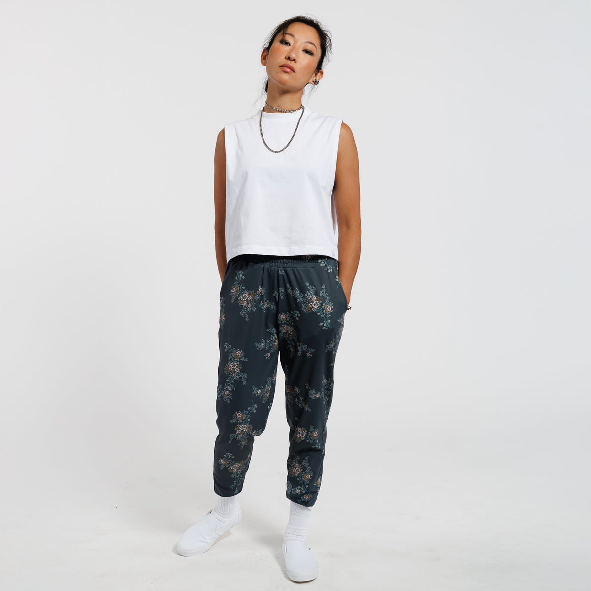 Person wearing a white sleeveless top and dark floral pants on a white background