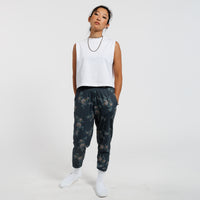 Person wearing a white sleeveless top and dark floral pants on a white background