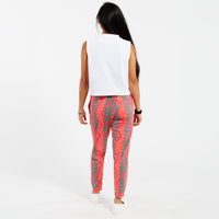 Woman wearing a white cropped tank top and pink patterned with green leaves pants on a white background