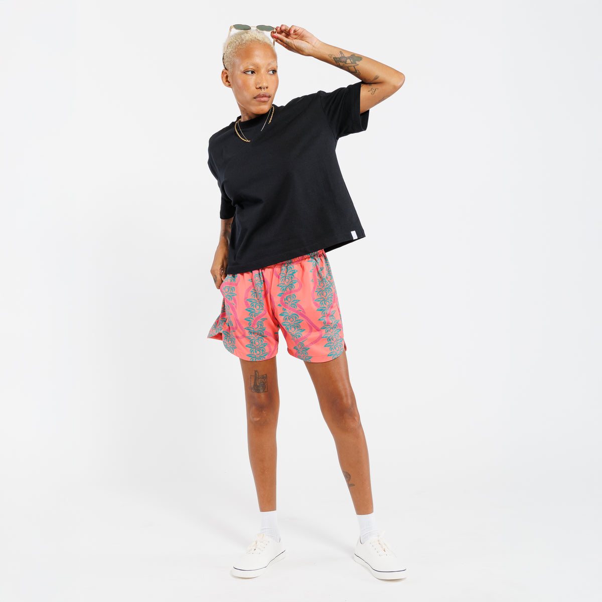 Person wearing a black t-shirt and pink shorts with a green leaves pattern on a white background
