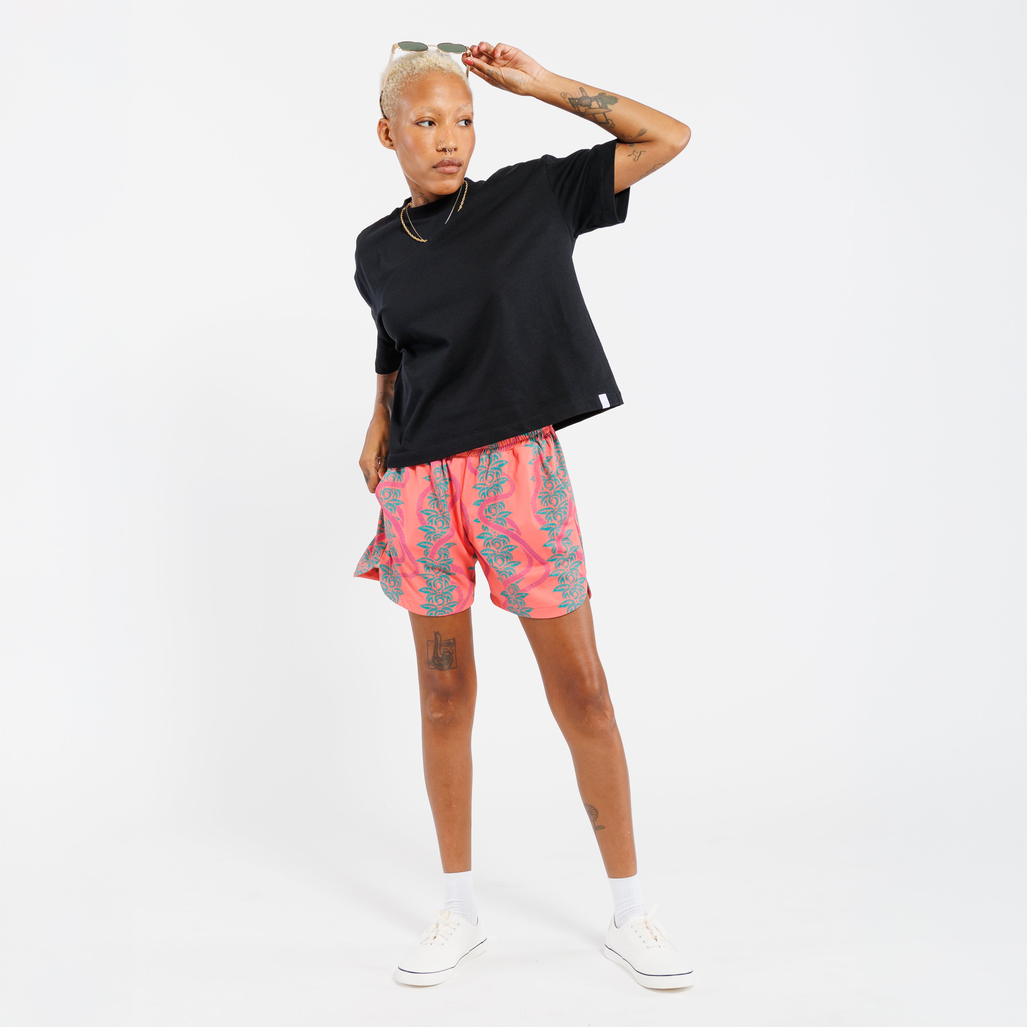 Person wearing a black t-shirt and pink shorts with a green leaves pattern on a white background