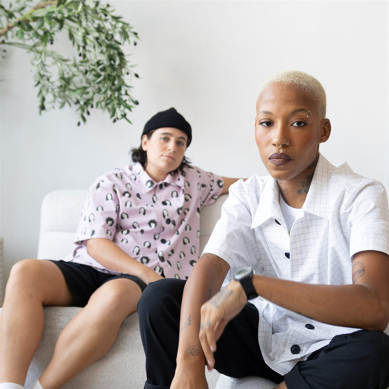 Two models on a white couch in a lilac print shirt and a white grid shirt