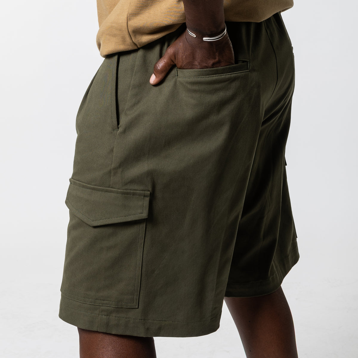 Close-up of olive cargo shorts from the side, showing the flap cargo pocket, back pocket and knee-length hem.