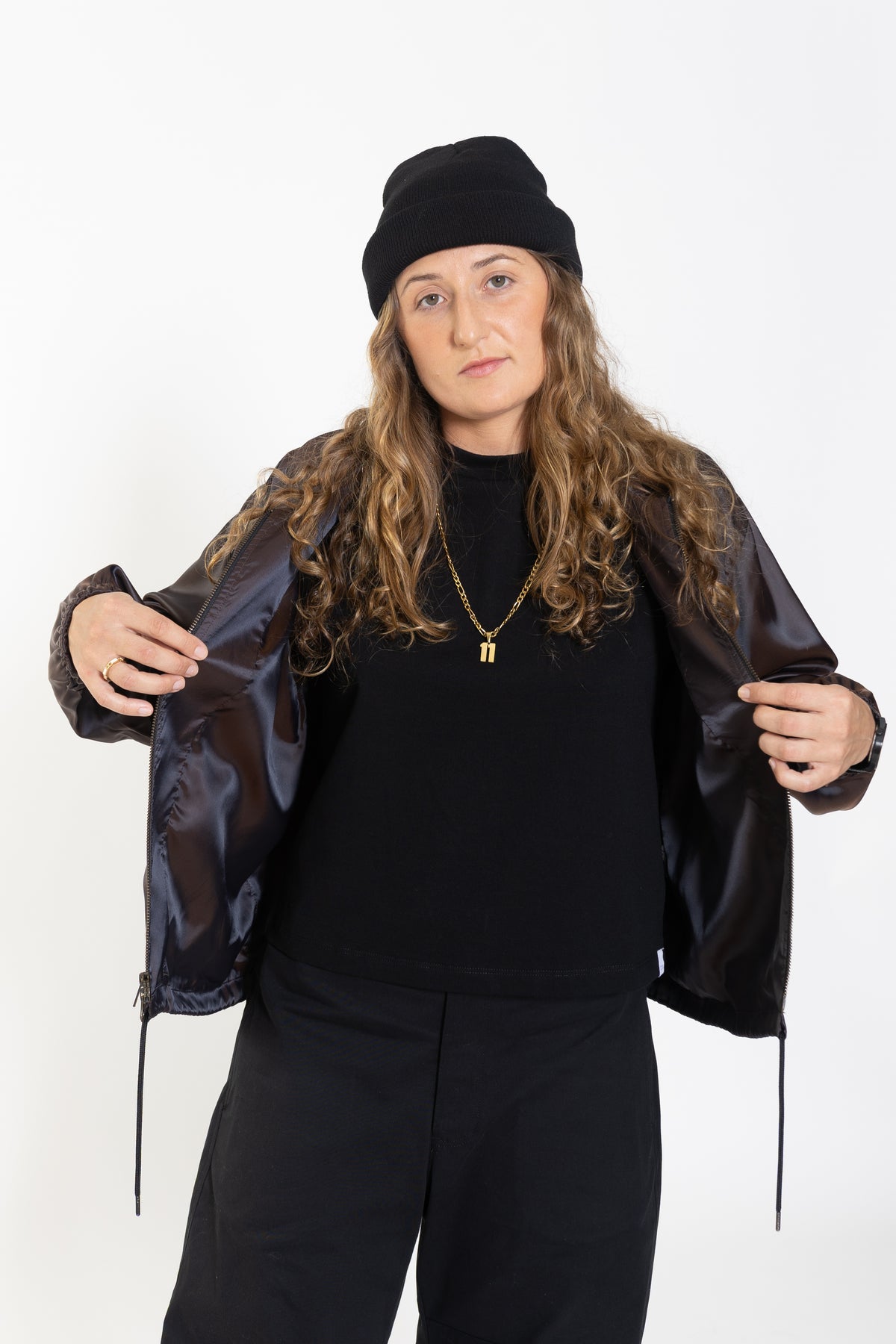 Woman holding open the Cher jacket in iridescent purple satin over a black top, looking at the camera.