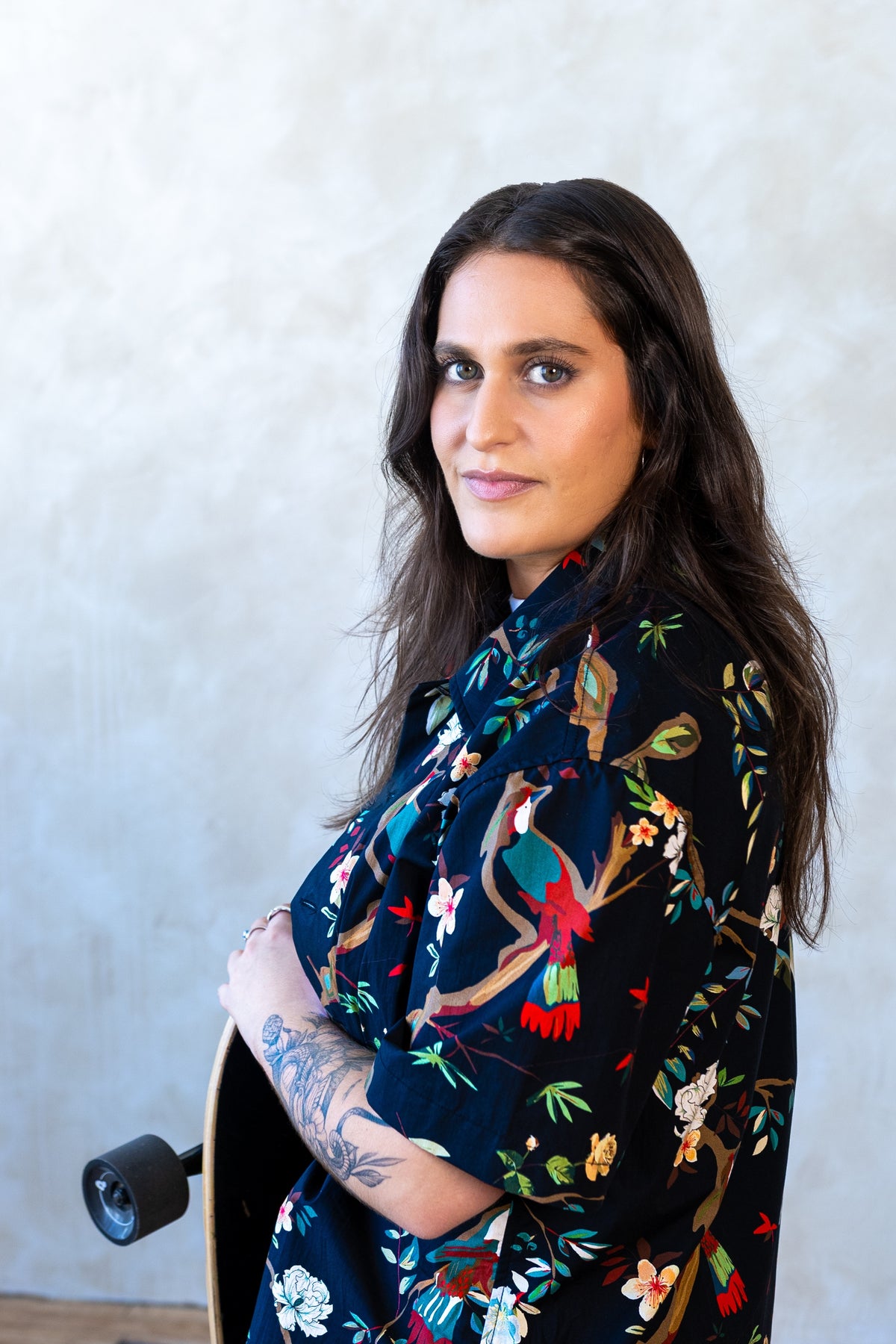 Woman in the Lala camp shirt in the Bird print, navy with tropical birds and flowers, holding a skateboard at her side.